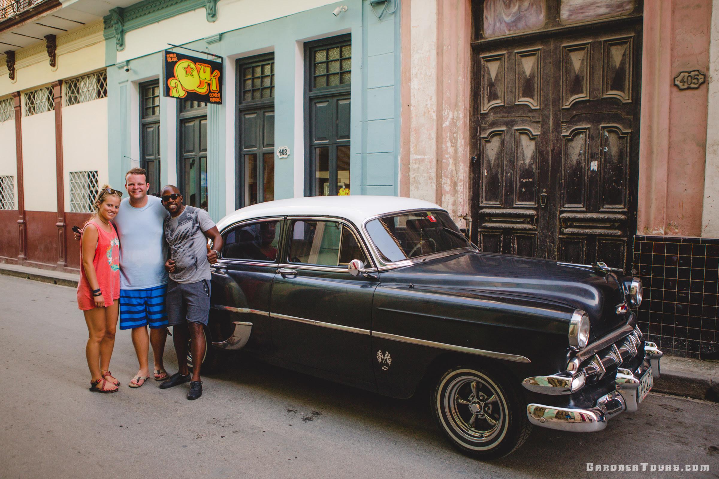 American Couple Posing for a photo with their Black Chevrolet Bel Air Classic Car Taxi Driver Michel in Havana, Cuba