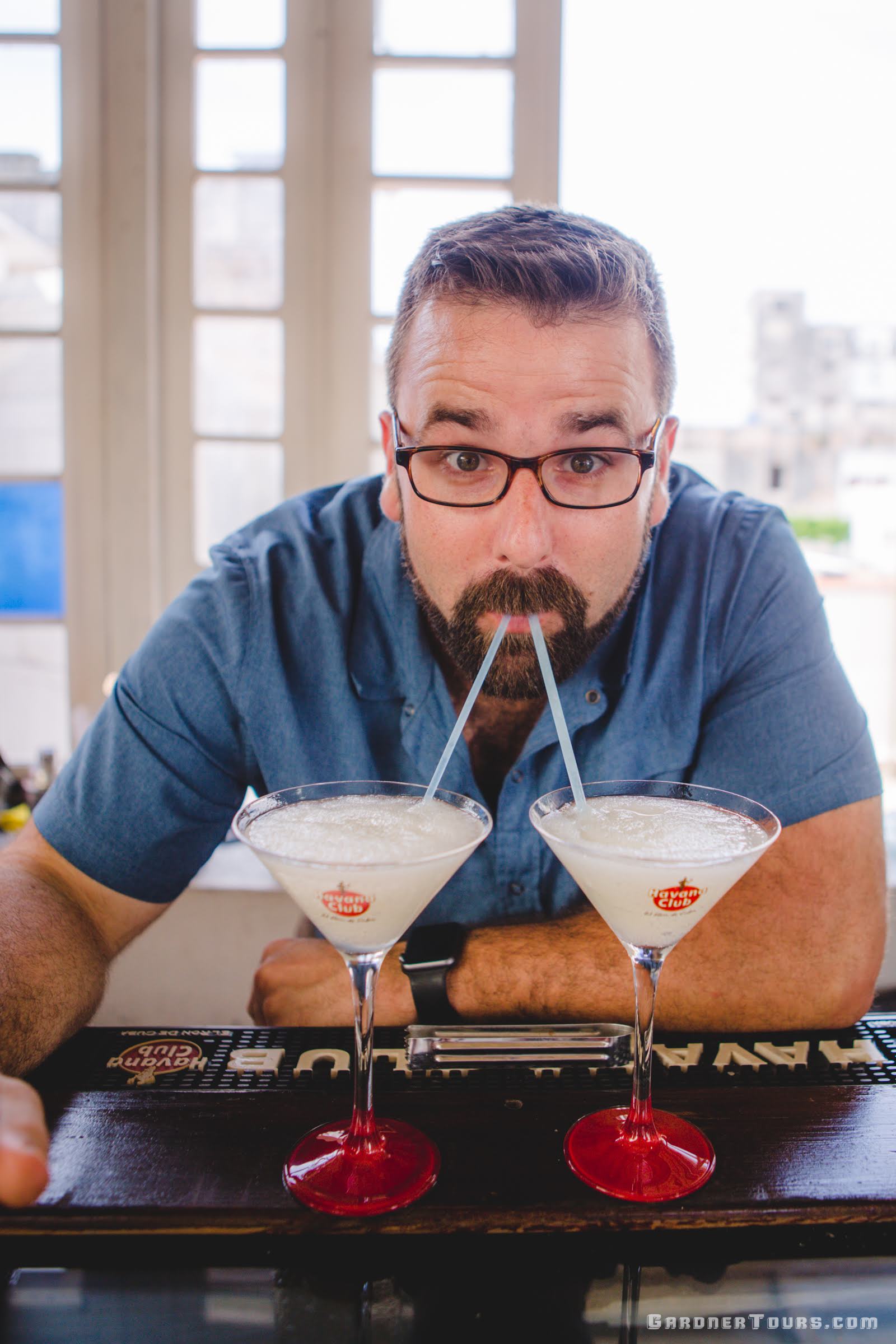 A Silly Man in a Blue Shirt Drinking two Frozen Daiquiris at one time on a Rooftop during a Cuban Cocktail Lesson in Old Havana, Cuba