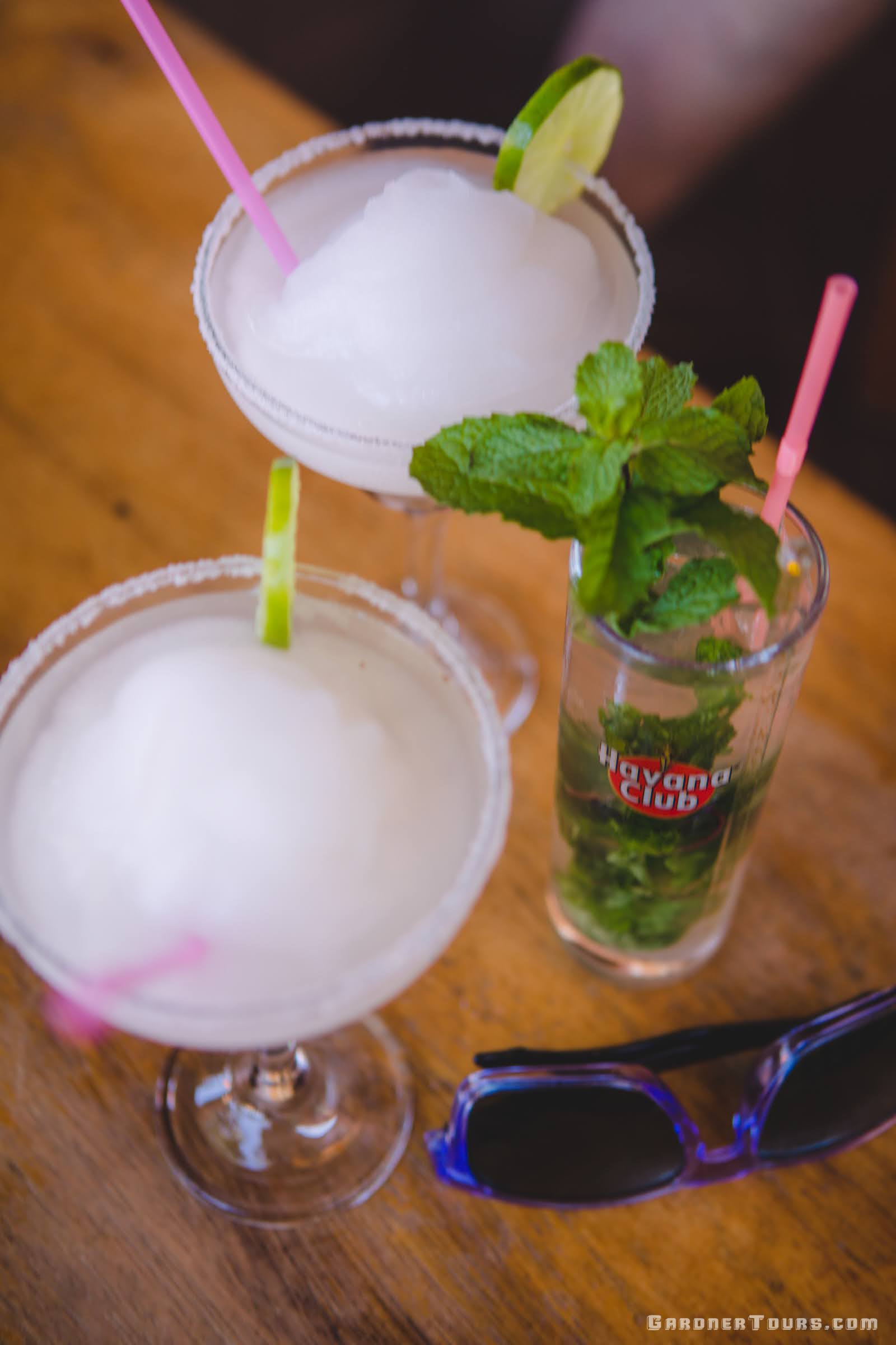 Two Frozen Daiquiris, a Mojito, and a pair of Blue Sunglasses on a Table at 3J Bar in Viñales, Cuba