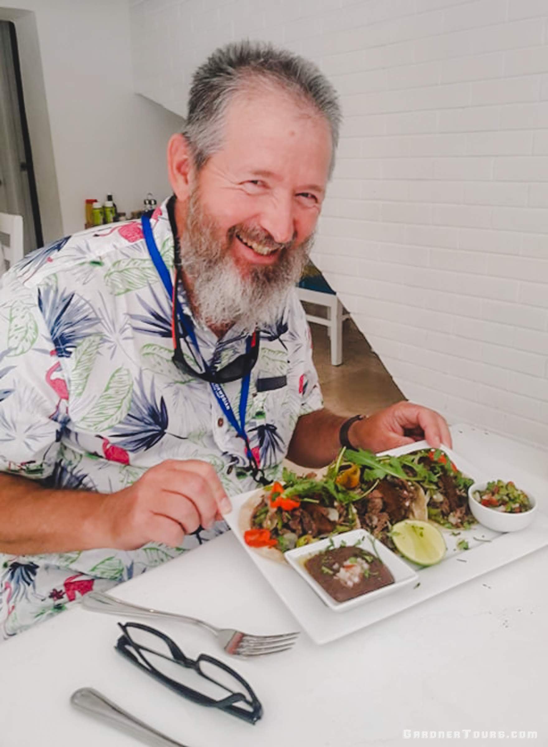 A man smiling as he eats three delicious tacos with vegetables and black beans at Restaurant Paladar Lo de Monik in Old Havana, Cuba