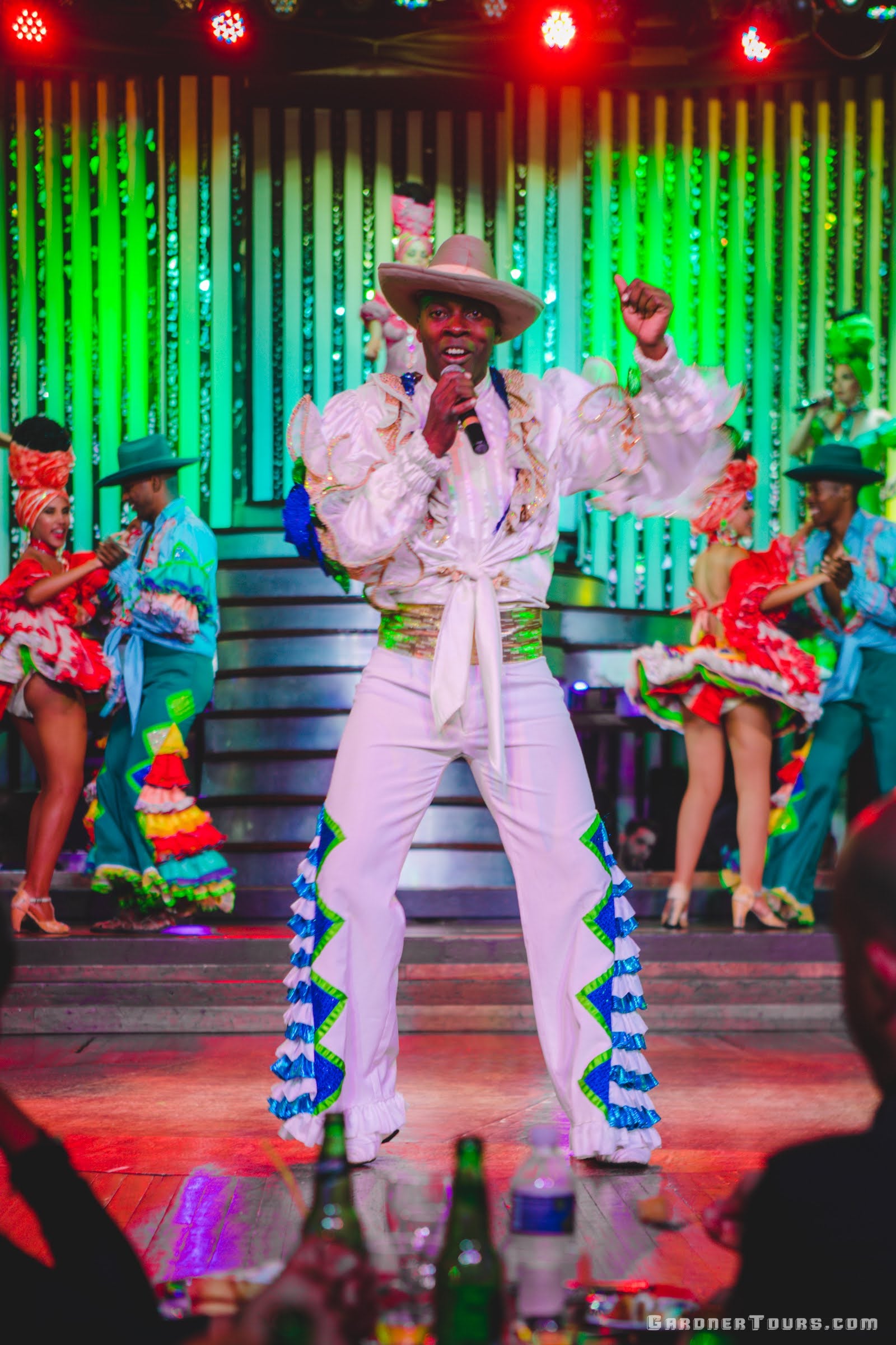 Lead male singer in cowboy hat and many dancers in colorful outfits performing at the Cabaret Parisien's Big Show in the Hotel Nacional in Havana, Cuba