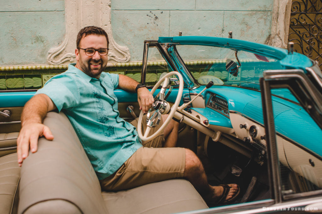 Colby Gardner owner of Gardner Tours wearing a shirt that matches the car color while sitting in a turquoise 1954 Mercury Convertible in Havana Cuba