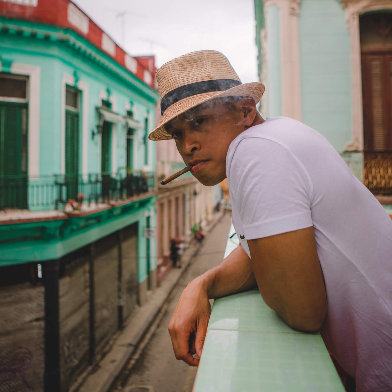 Gardner Tours Premium Cuba Cigar Tour Man wearing a fedora leaning over the balcony in Old Havana as he smokes a Cuban Cigar