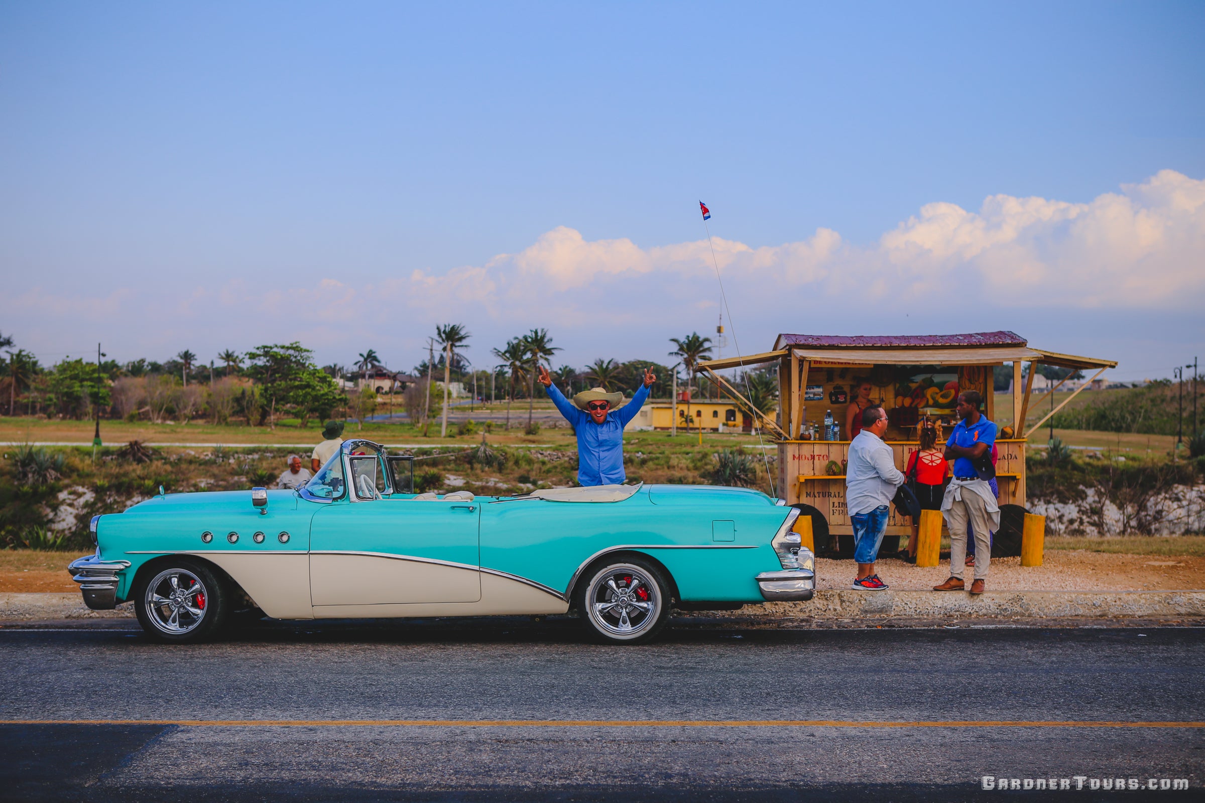 Cuban Man driving Turquoise Buick Classic Car and Posing with Arms in the Air near El Morro Castle in Havana, Cuba