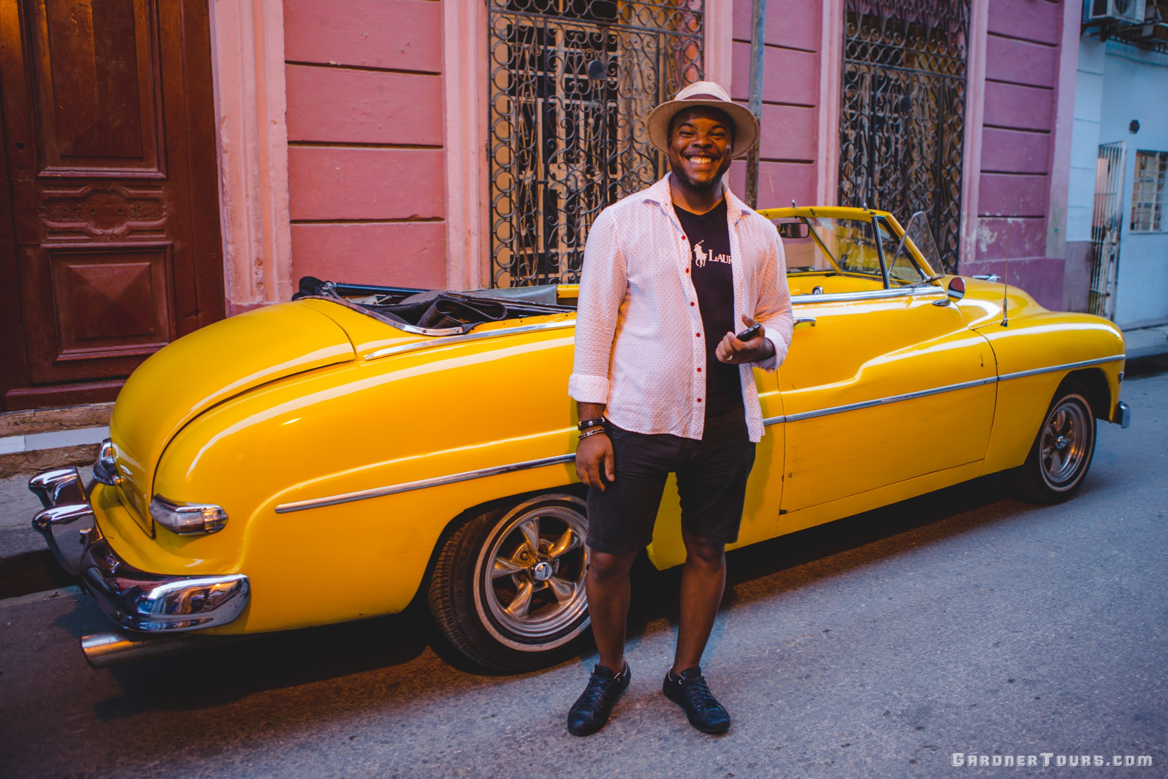 Gardner Tours Cuban Tour Guide Michel smiling and standing in front of a yellow classic car in Havana, Cuba