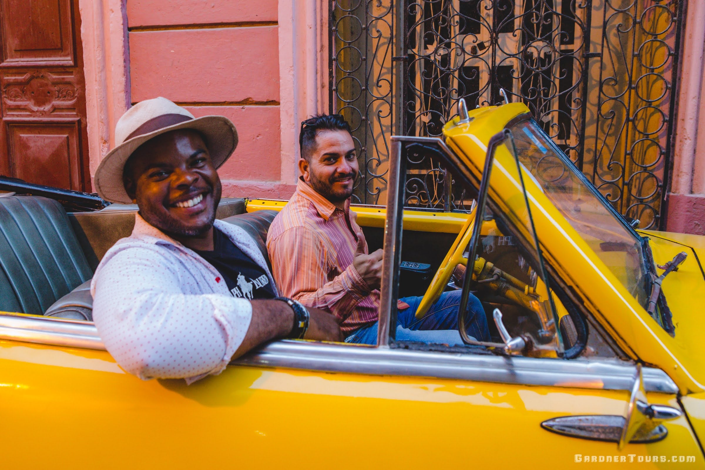 Gardner Tours Cuban Tour Guide Michel smiling with a driver in a Yellow Classic Car in Havana, Cuba