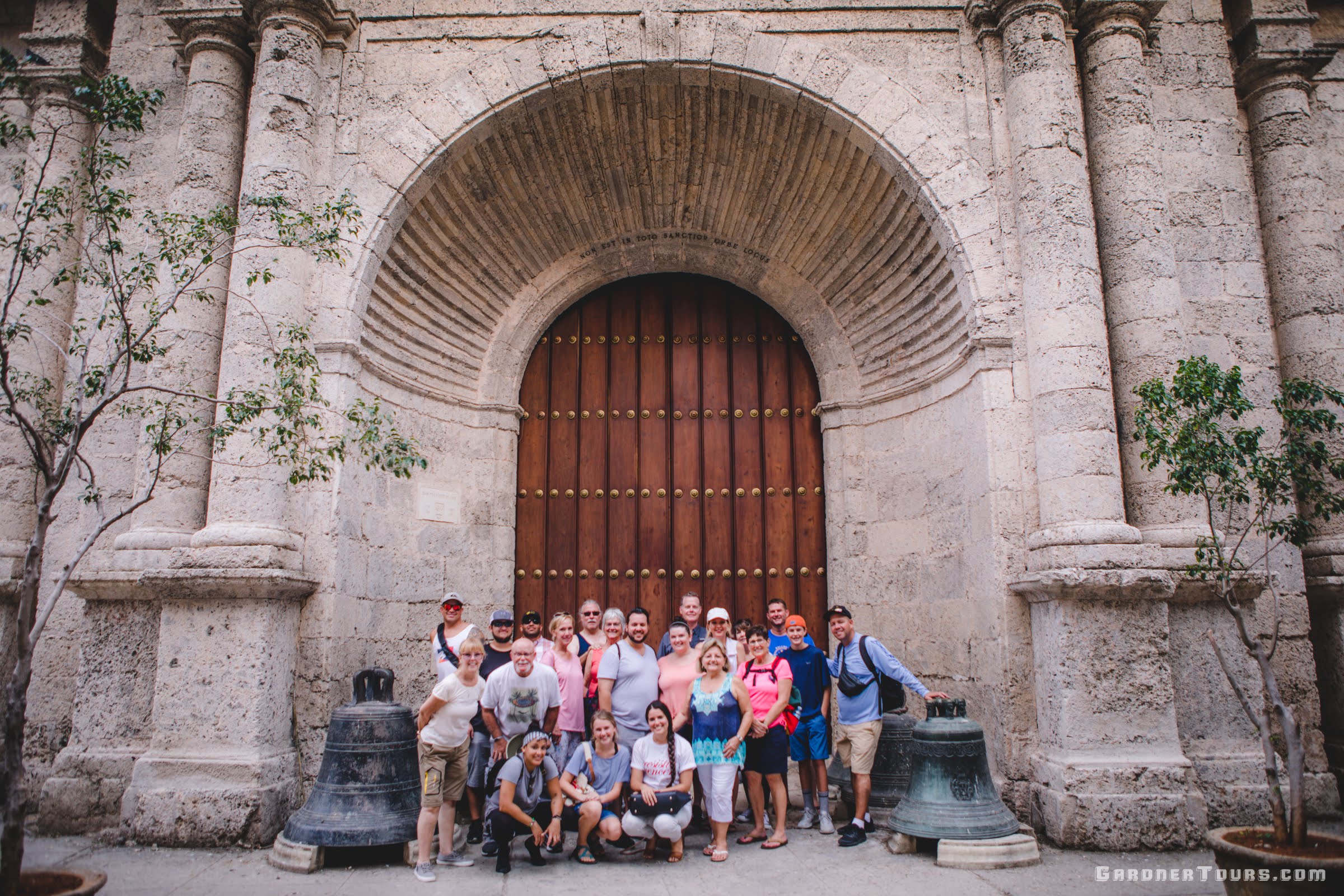 Gardner Tours Cuban Tour Guide Yunior with a large group of travelers from the USA in Old Havana Cuba by the big door of the Convent of San Francisco de Asis