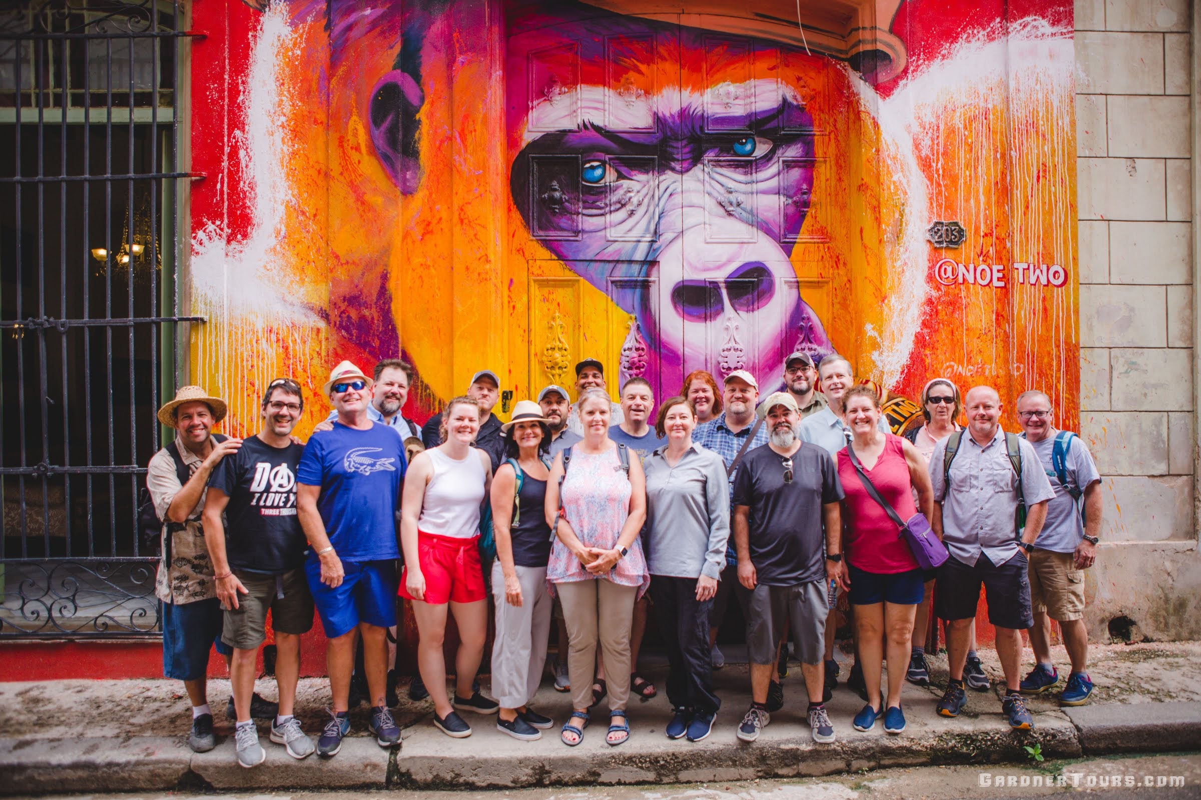 Gardner Tours Cuban Tour Guide Yunior posing with a group of twenty travelers in front of the noe_two gorilla painting on Calle Havana in Old Havana, Cuba