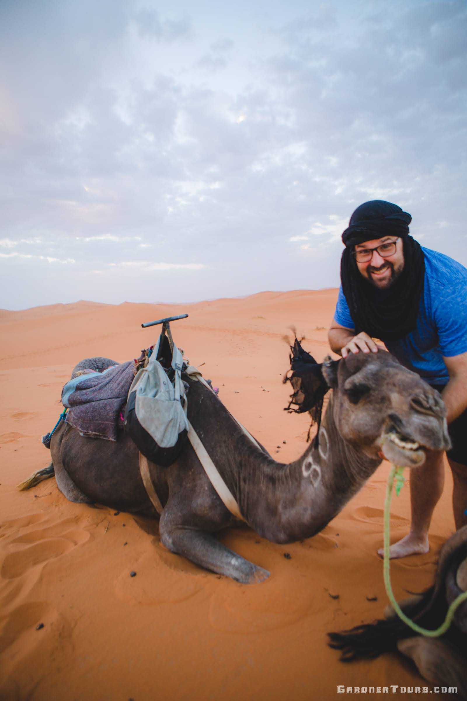 Gardner Tours Owner and Tour Guide Colby Gardner being funny and smiling with one of the camels in the Sahara Desert in Morocco