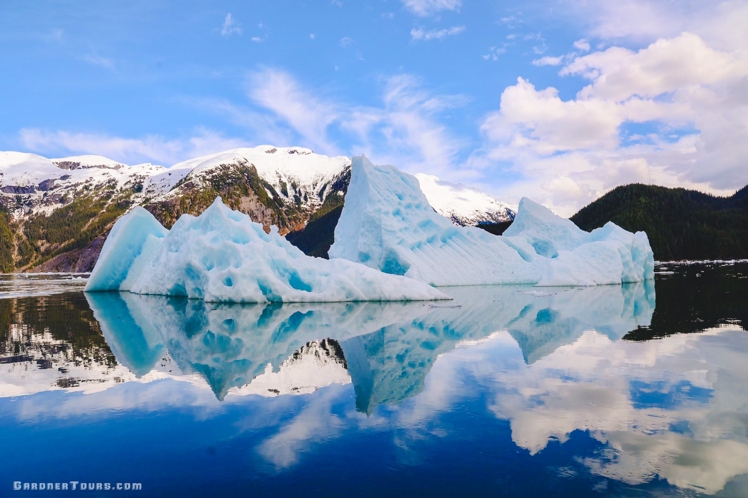 Massive bright blue icebergs reflecting in the calm waters of an Alaskan glacial fjord.