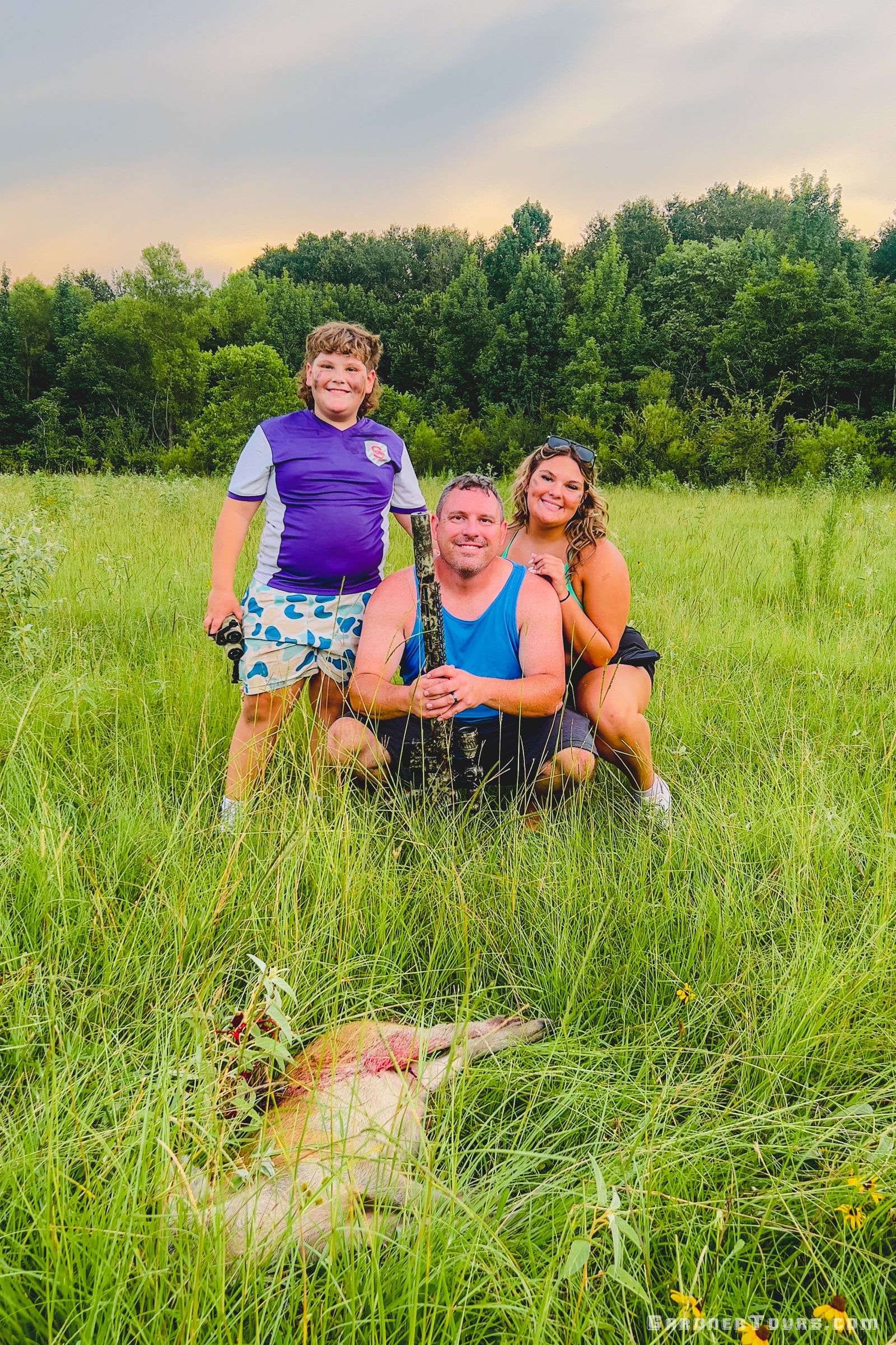 A family of three smiling in a grassy field with their rifle after a successful daytime hog hunt in Centerville, Texas.