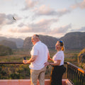 A sweet couple on their Luxury Cuba Tour, with Gardner Tours, wearing matching white outfits and laughing while enjoying the sunset at the Los Jazmines Viewpoint overlooking the Vinales Valley in Vinales Cuba.