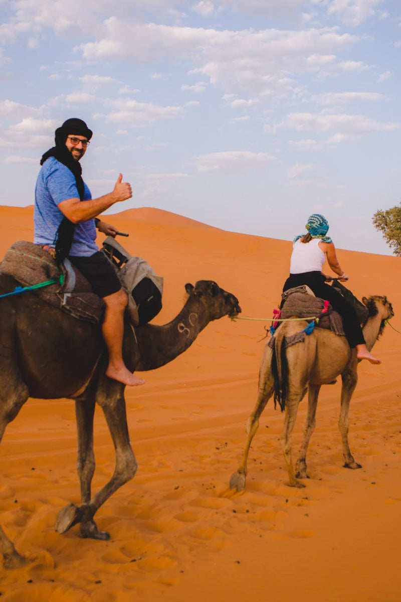 Colby Gardner giving a thumbs-up during a guided camel trek through the desert dunes in Morocco - vertical photo