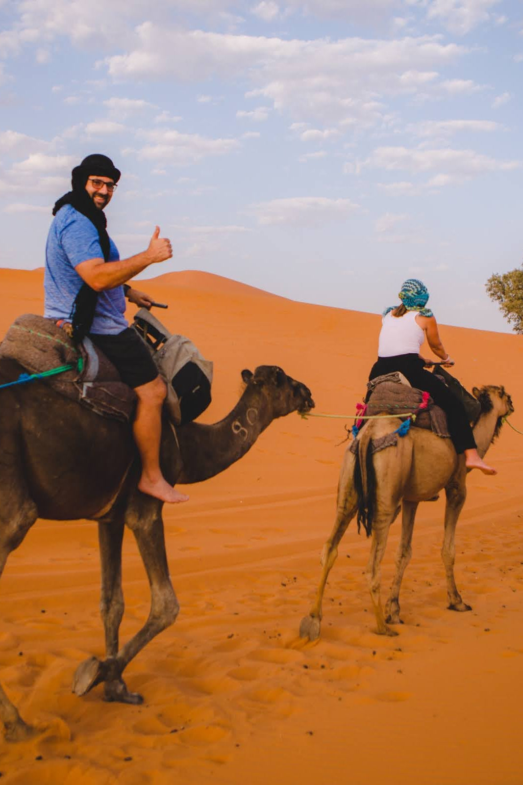 Colby Gardner giving a thumbs-up during a guided camel trek through the desert dunes in Morocco - vertical photo