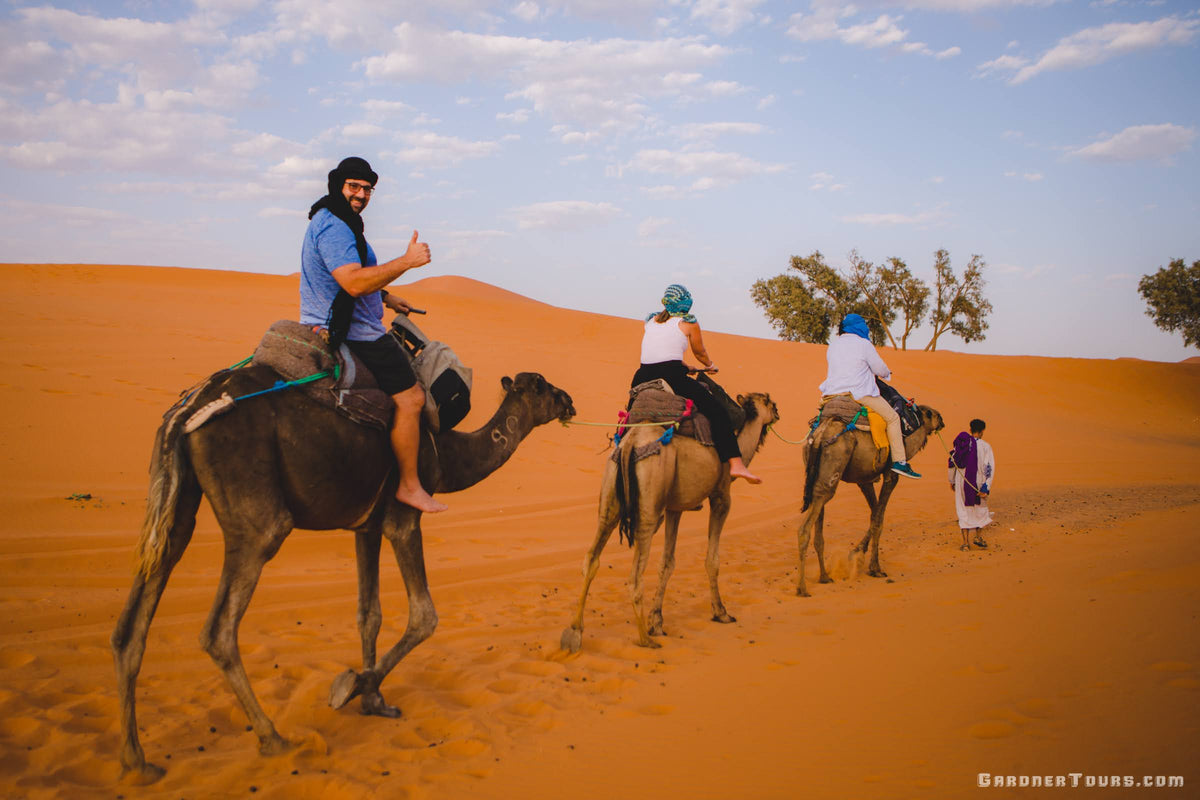 Colby Gardner giving a thumbs-up during a guided camel trek through the Sahara Desert dunes in Morocco