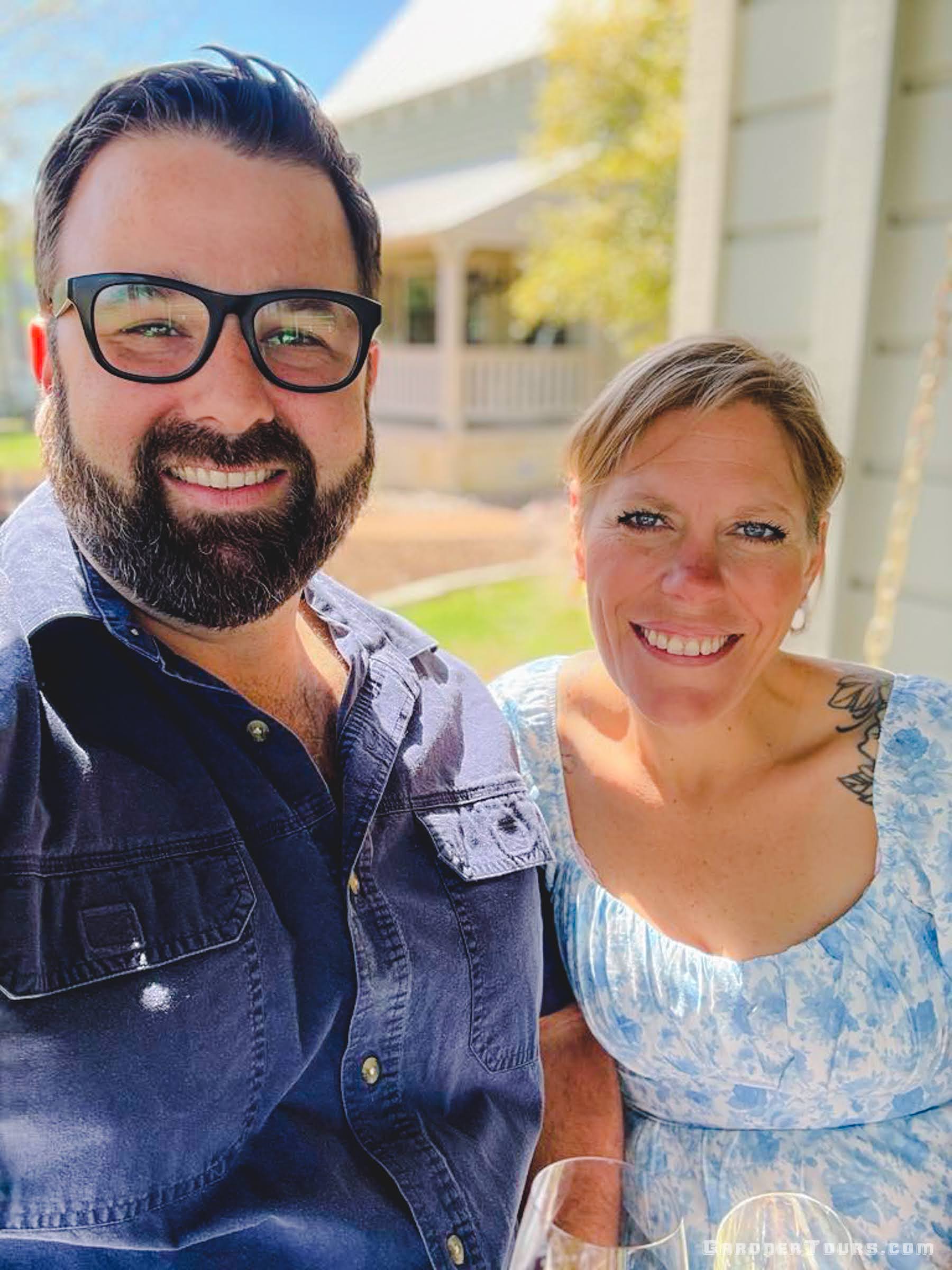 Two people smiling outdoors with a clear sky and building in the background