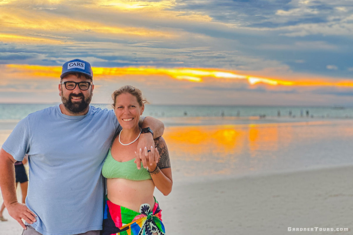 Couple standing on a beach at sunset with colorful sky