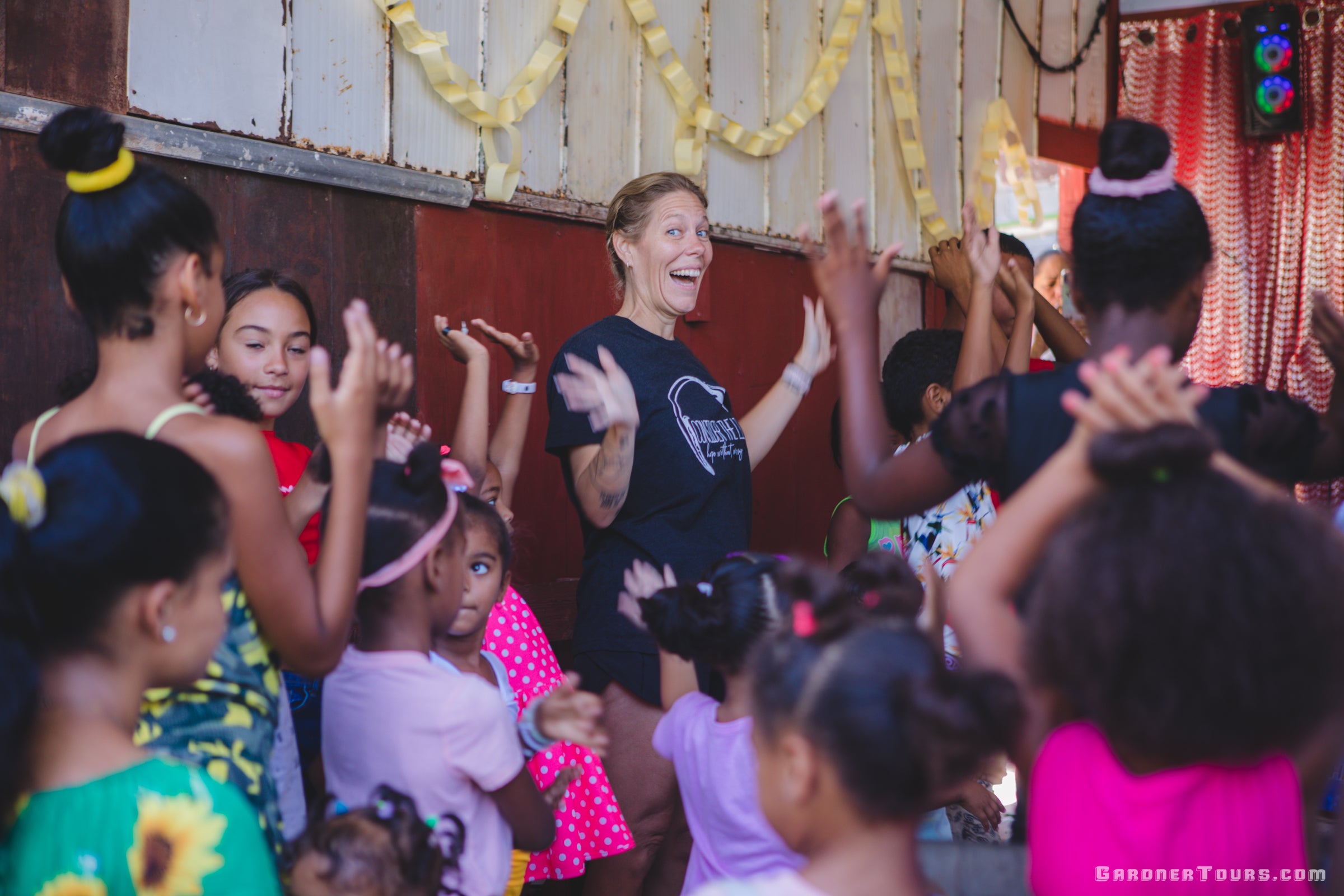 Woman in a black t-shirt interacting with children in a lively indoor setting