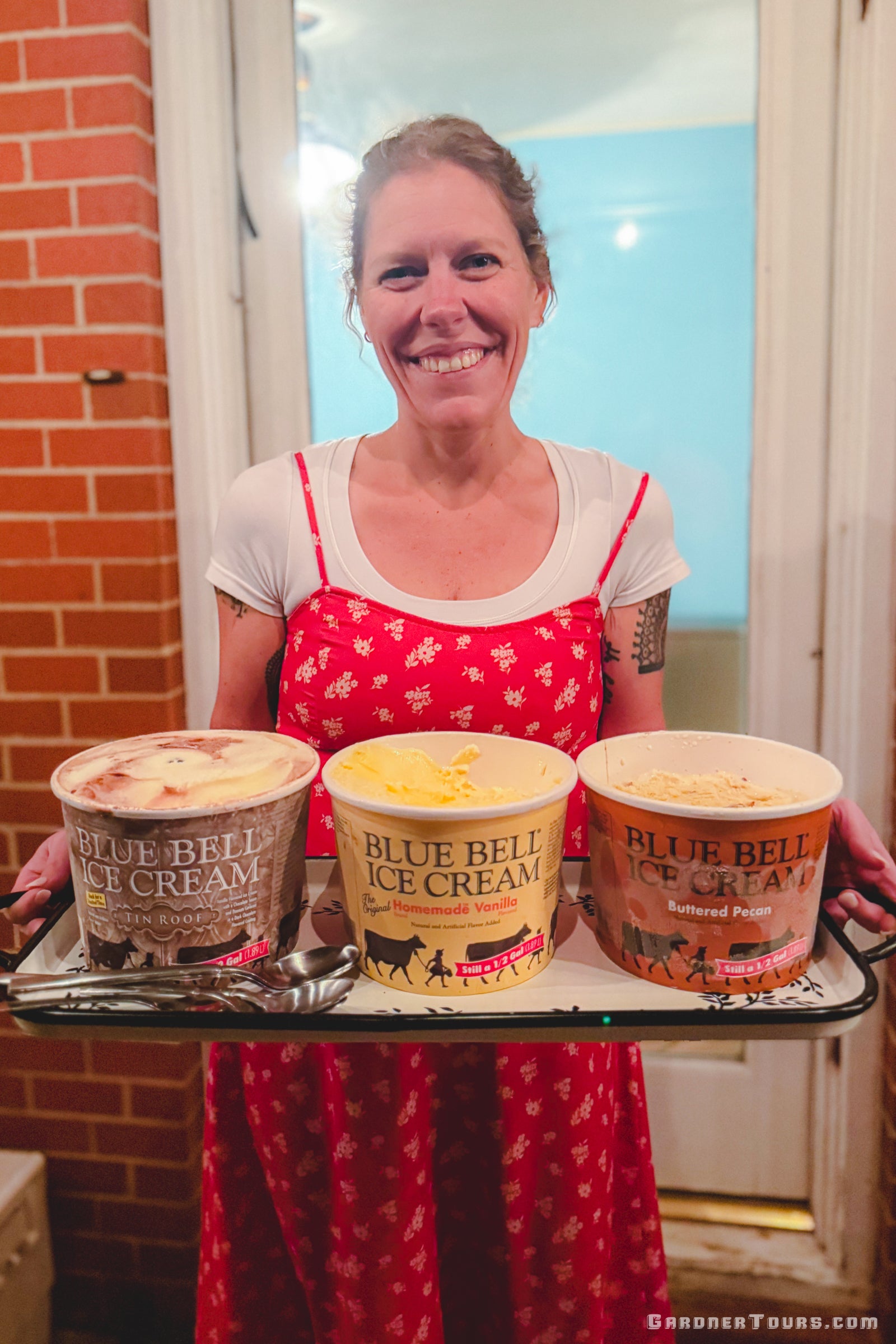 Woman in red dress holding a tray with three containers of Blue Bell ice cream on a back porch in Centerville Texas.