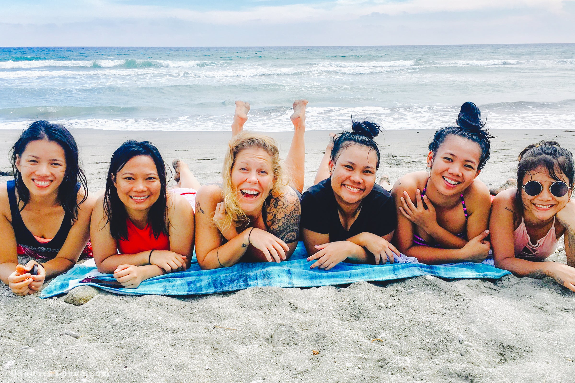 Group of six friends lying on a towel at the beach