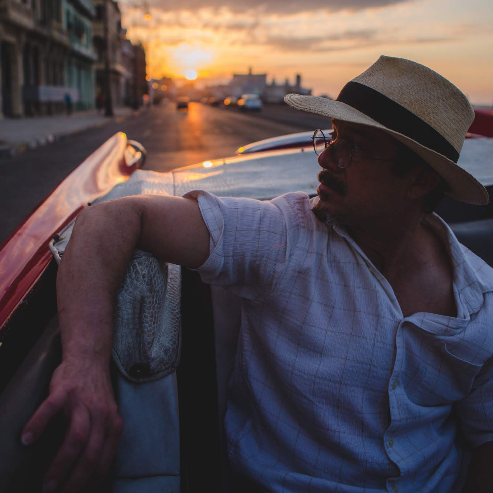 Man wearing a white shirt and Panama Jack hat riding in a classic car in Havana at sunset while on his Premium Cuba Cigar Tour with Gardner Tours.