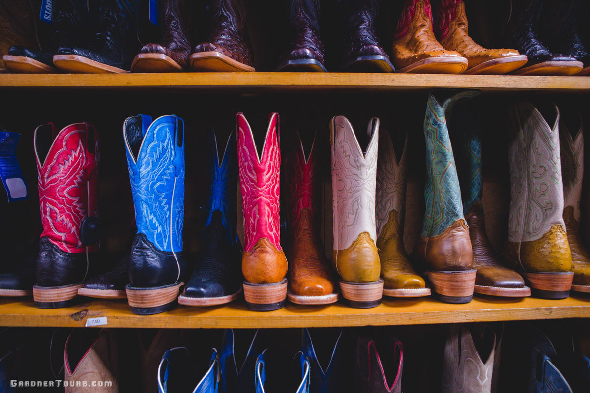 A colorful row of hand-crafted leather cowboy boots on display on wooden shelves in Fredericksburg, Texas