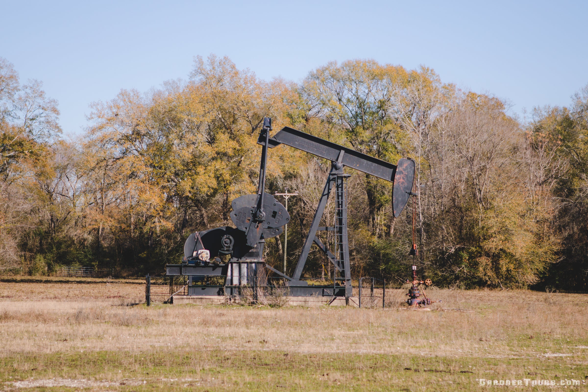 Oil pumpjack in a field with trees in the background