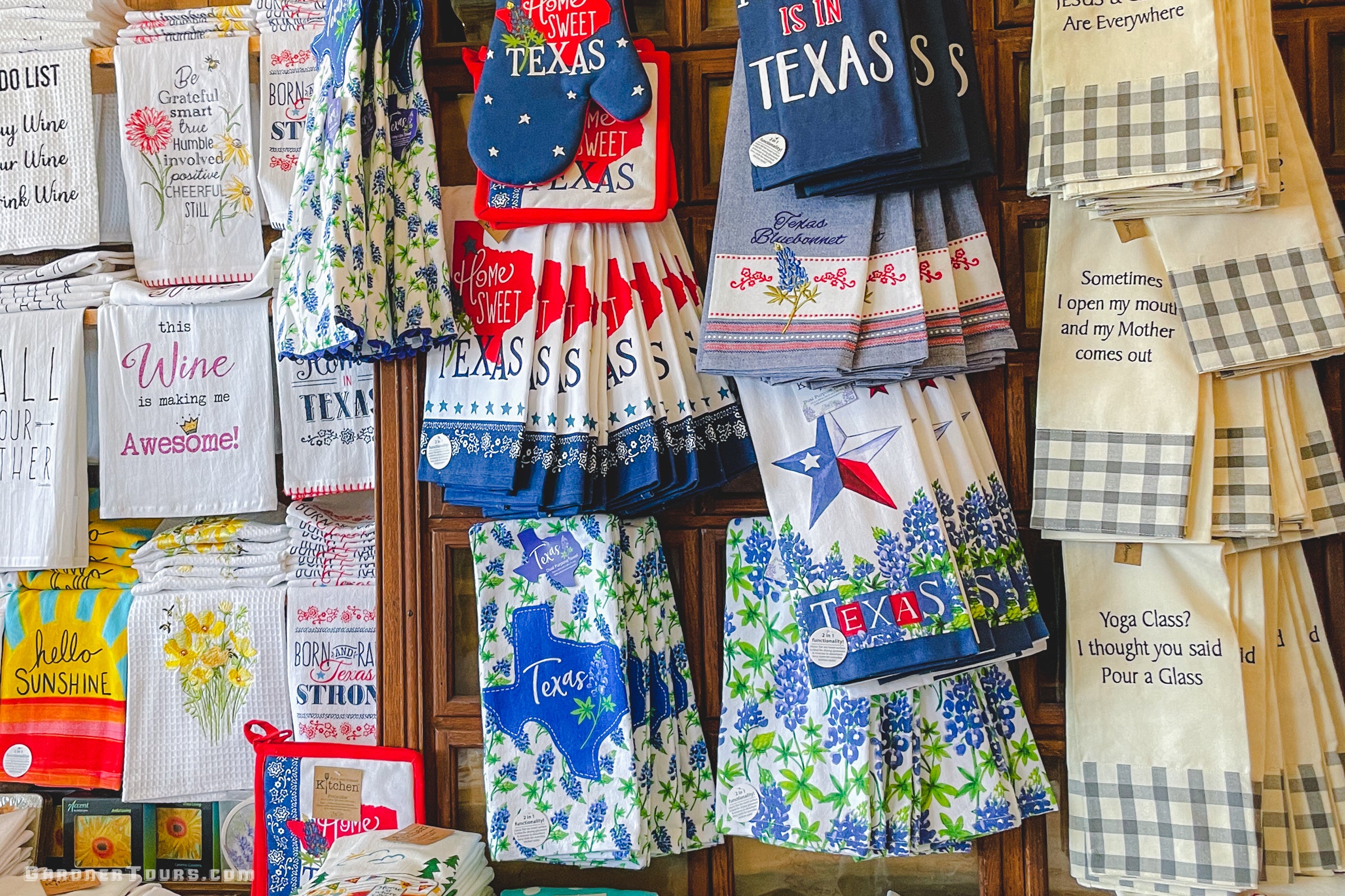 Collection of Texas-themed kitchen towels and aprons on a wooden rack.