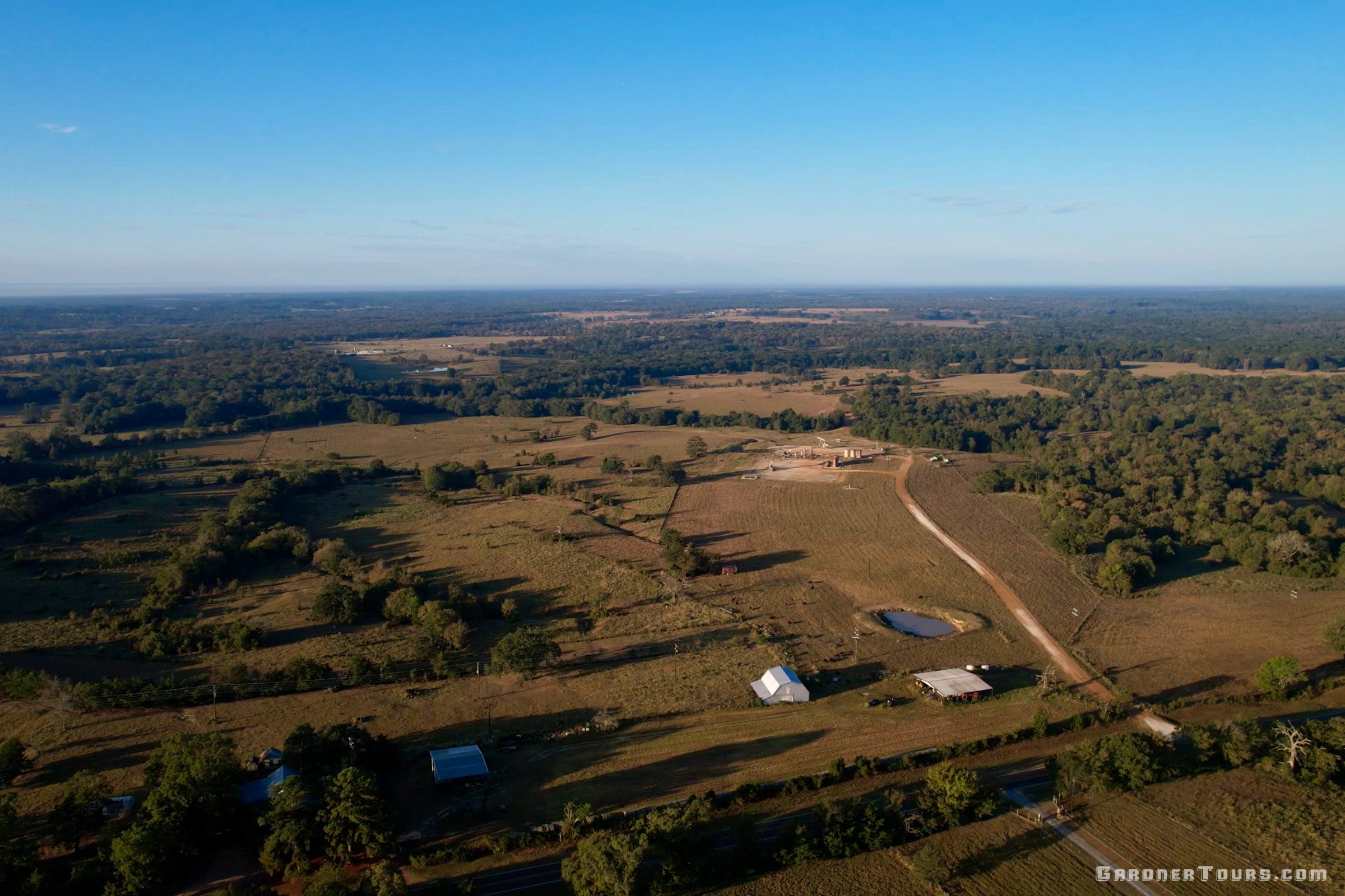 Aerial view of a rural landscape in Centerville, Texas with fields, trees, and buildings under a clear blue sky.