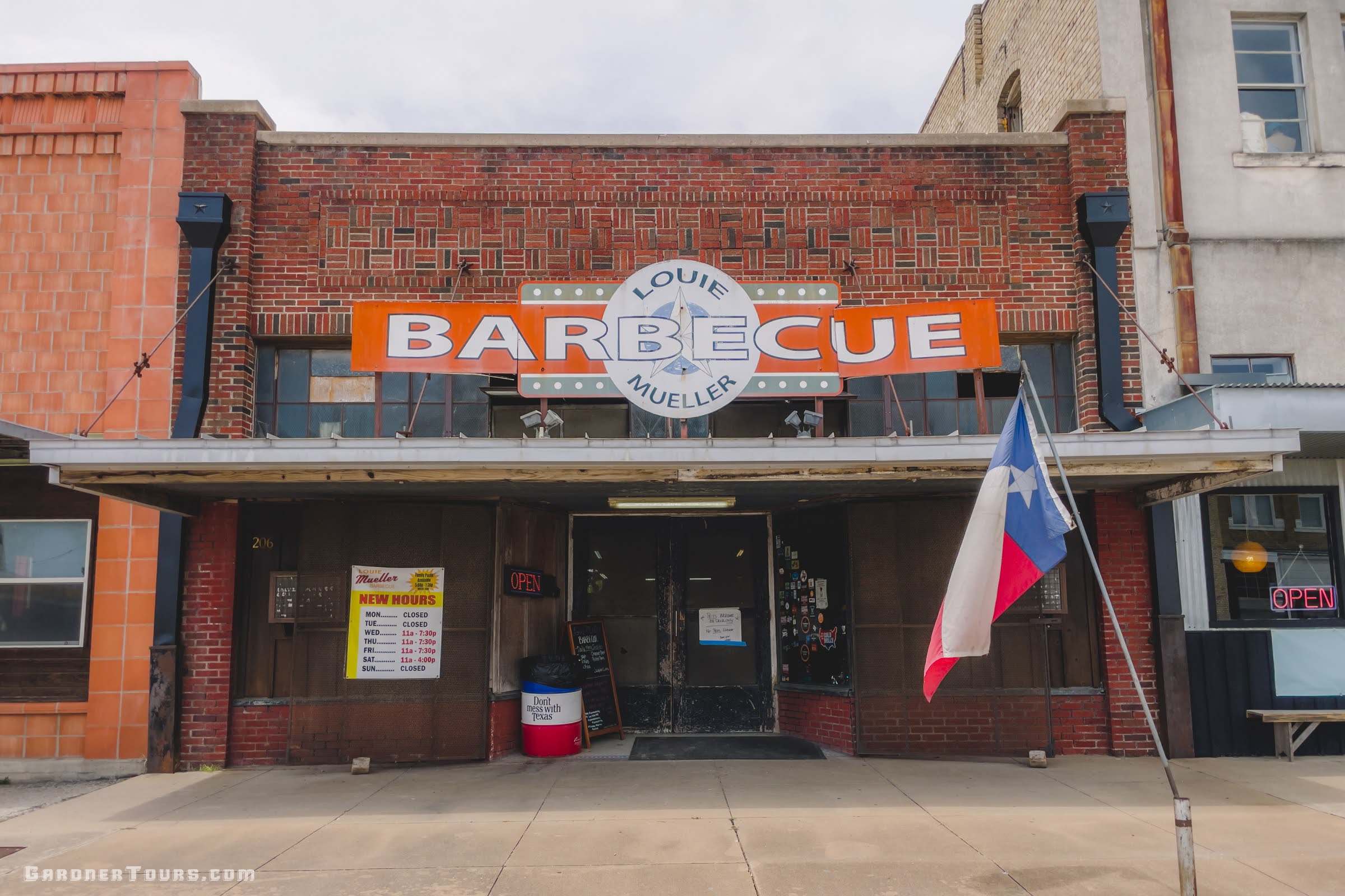 Louie Mueller Barbecue restaurant in Taylor, Texas with a sign and Texas flag in front of a brick building