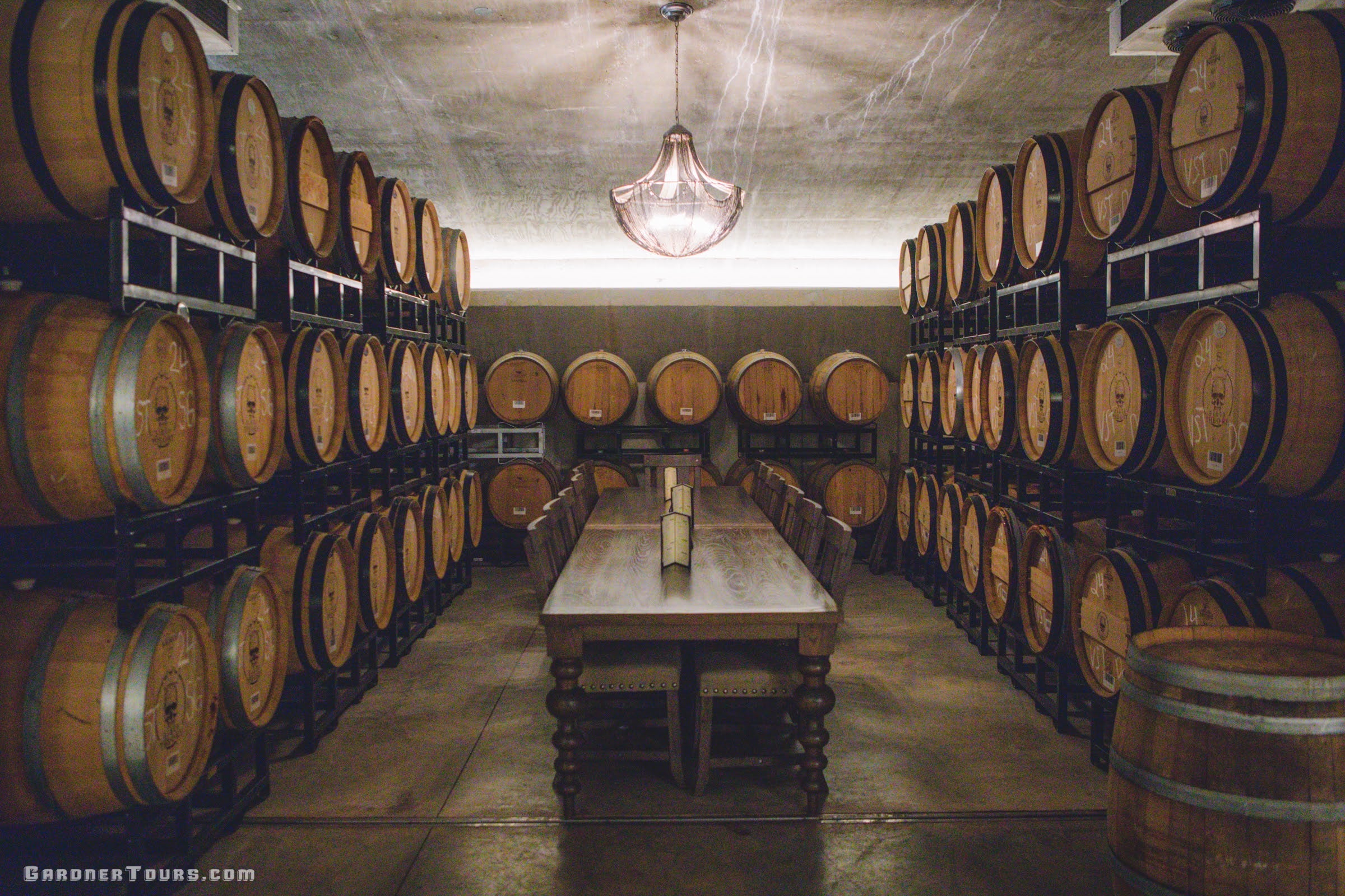 Wine cellar with wooden barrels and a long table in the center.
