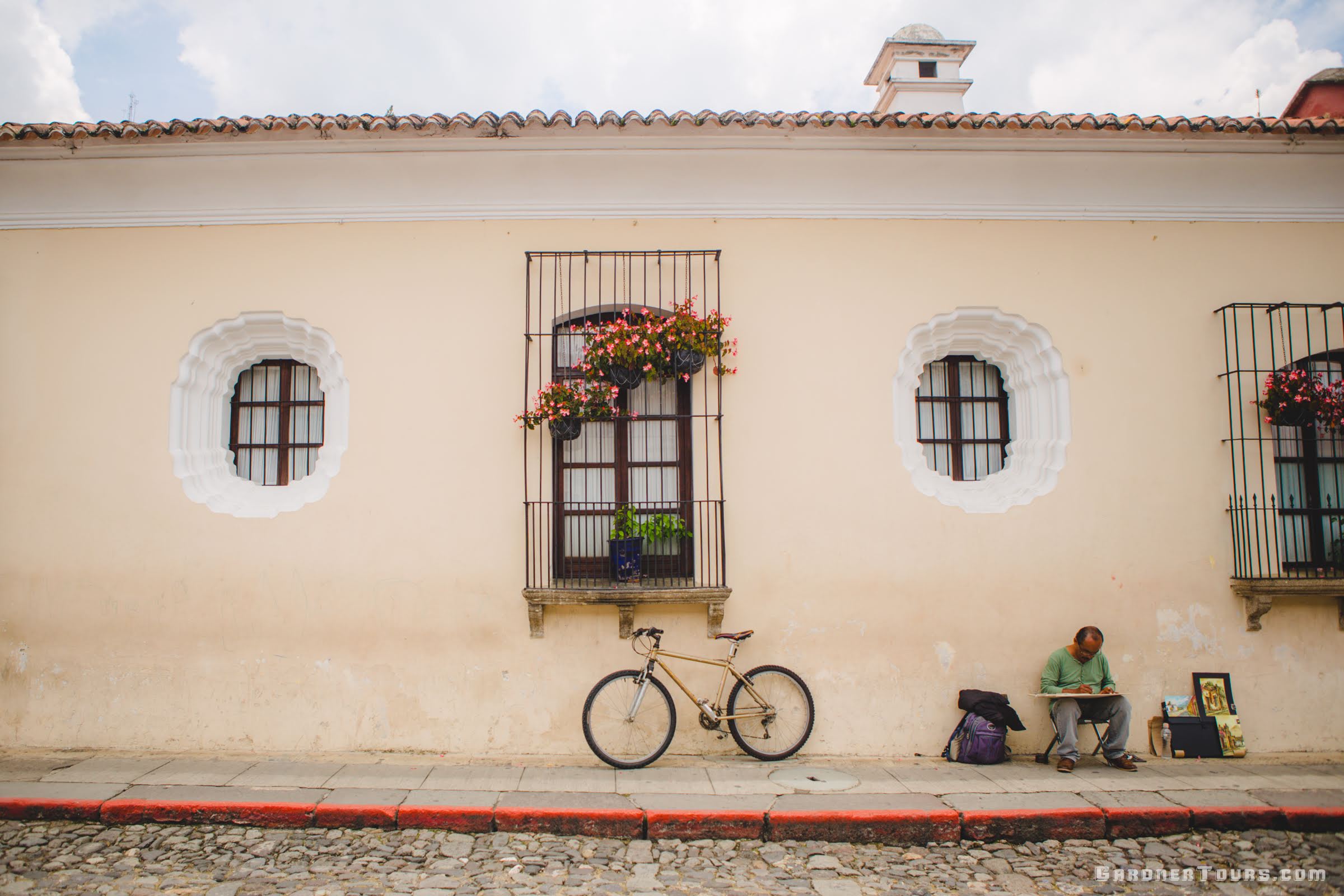 Beautiful Street with Bicycle Leaning against a House and an Artist painting while sitting on a stool in Antigua, Guatemala