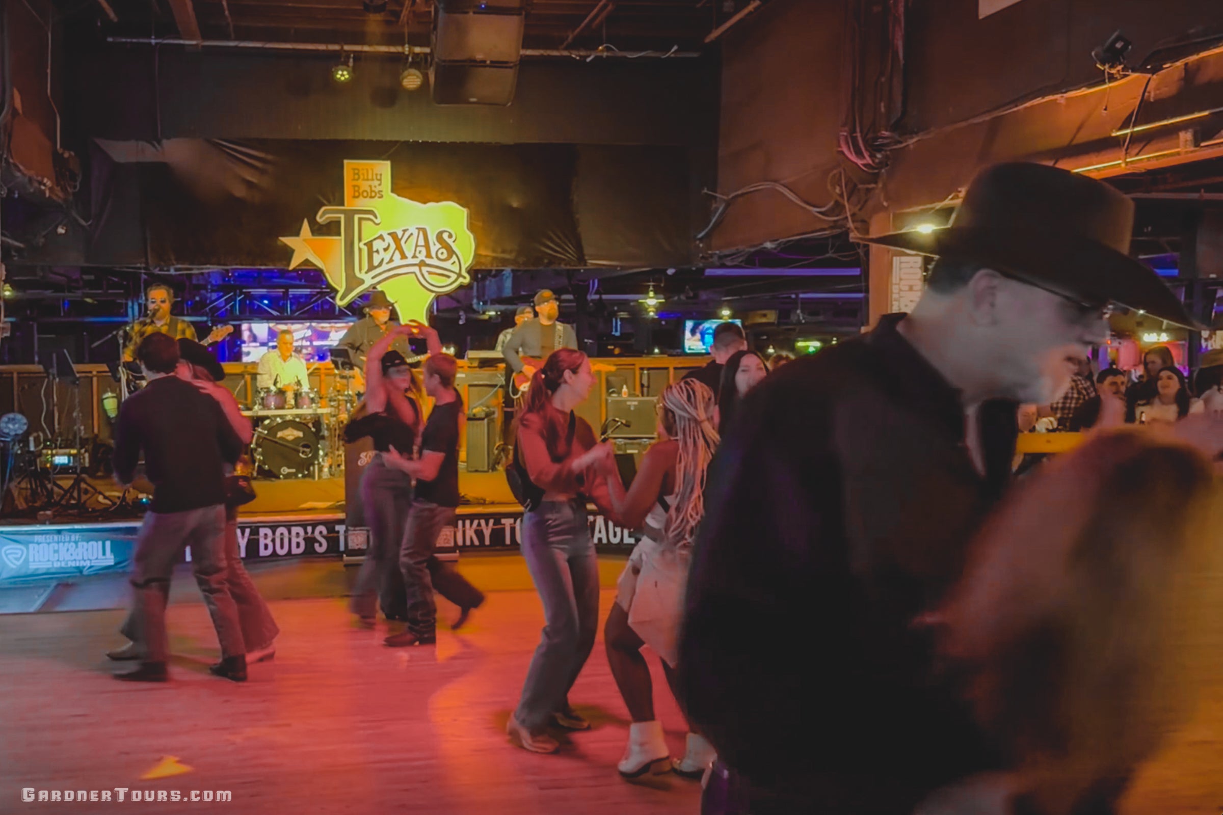 People dancing in a lively bar, Billy Bob's Texas in Fort Worth, Texas, with a neon sign in the background