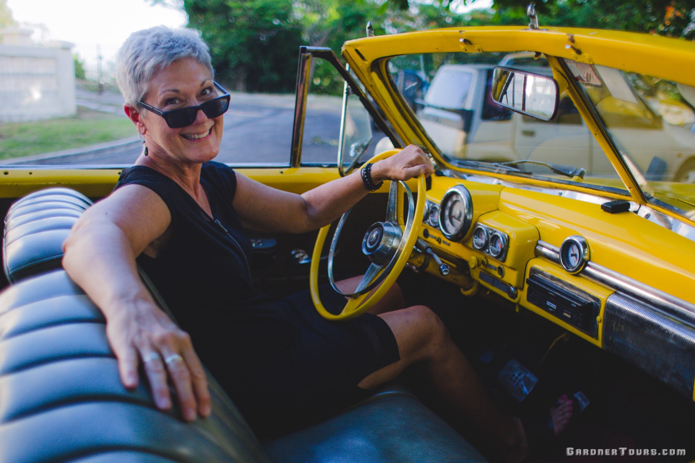 Gardner-Tours Custom Cuba Tours Woman Cindi Elder Driving Yellow Classic Car in Havana Cuba