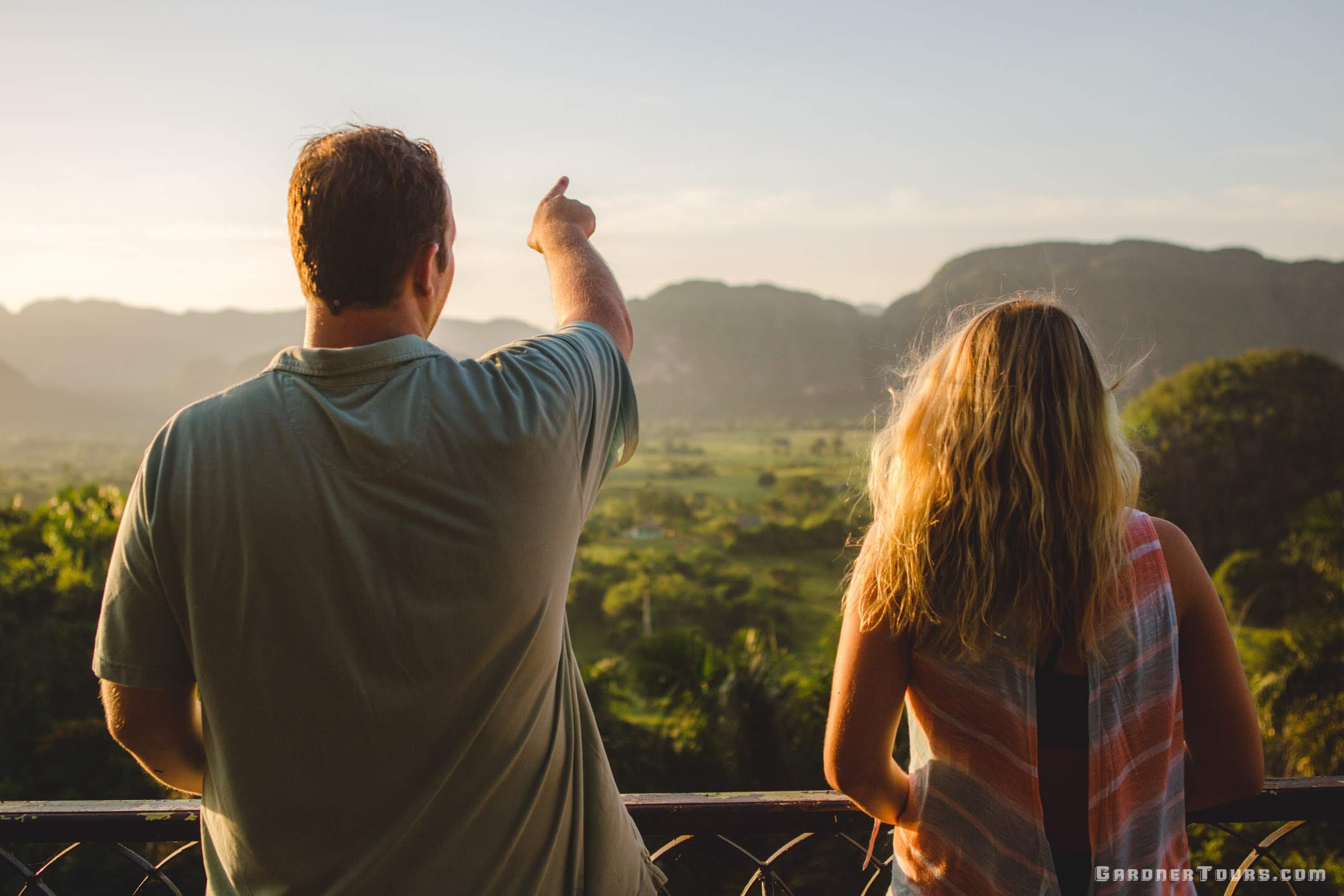 Man Points out over the VIñales Valley with a woman standing next to him at sunset. They are at the Hotel Los Jazmines Viewpoint in Viñales, Cuba