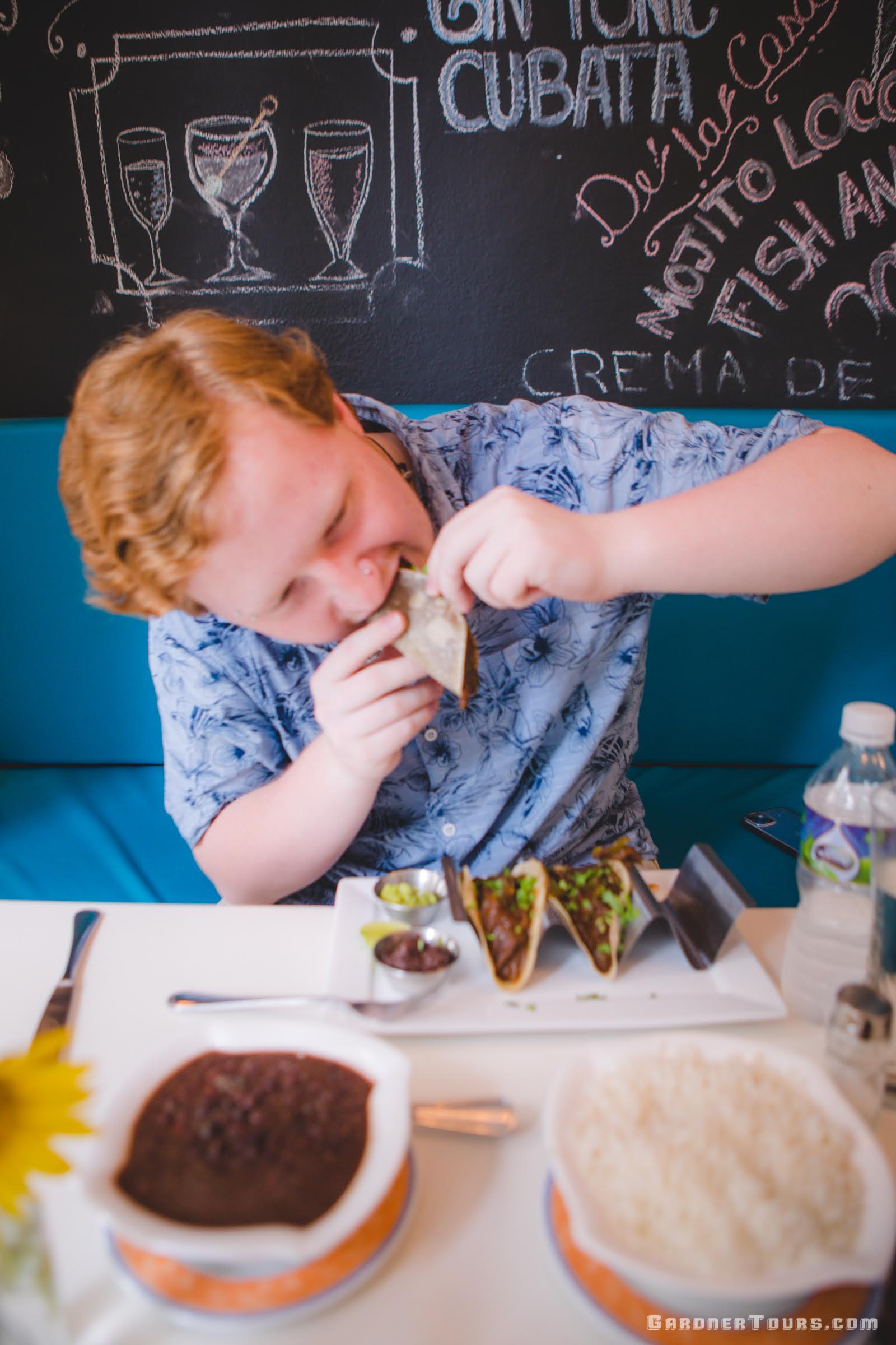 A young red headed man actively eating delicious tacos with vegetables, Cuban black beans and rice at Restaurant Paladar Lo de Monik in Old Havana, Cuba
