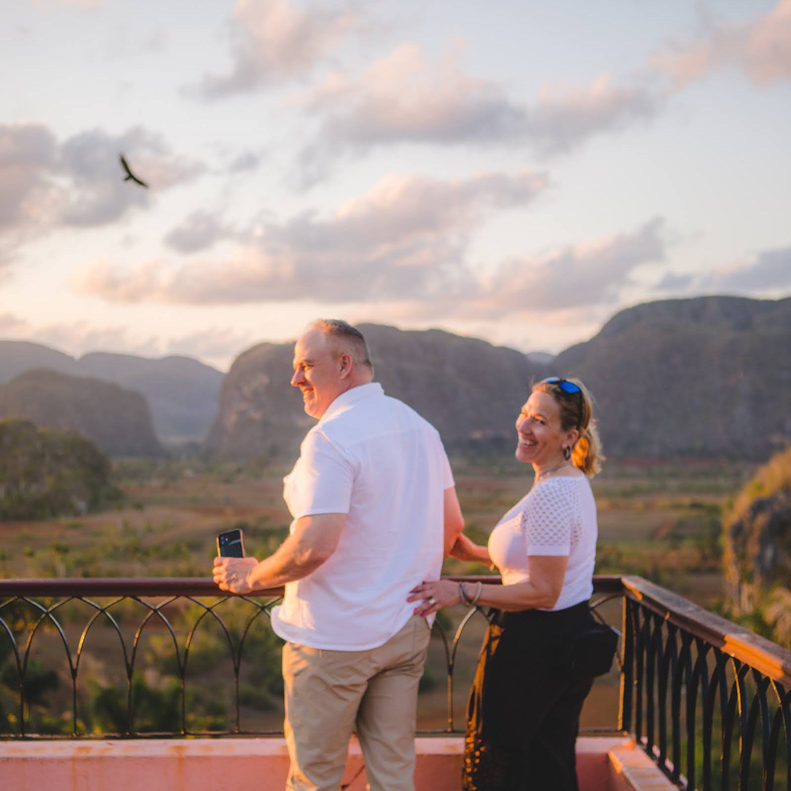 A sweet couple on their Luxury Cuba Tour wearing matching white outfits and laughing while enjoying the sunset at the Los Jazmines Viewpoint overlooking the Vinales Valley in Vinales Cuba