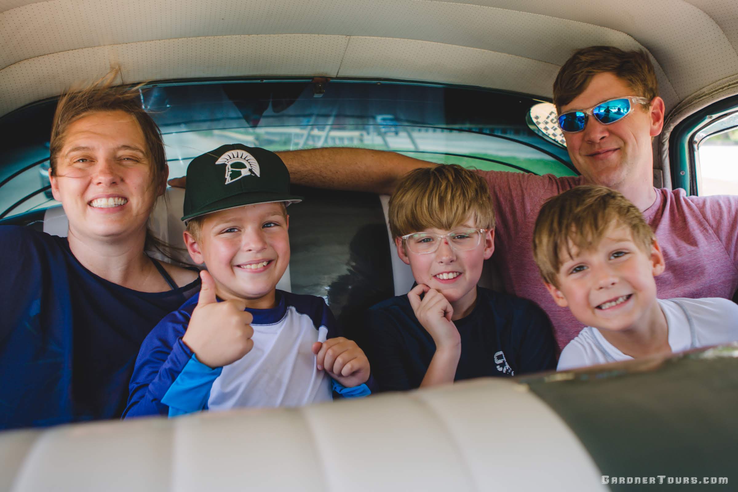 A beautiful family with mother father and three young boys smiling as they ride in the back seat of a classic car in Cuba on the way to the beach