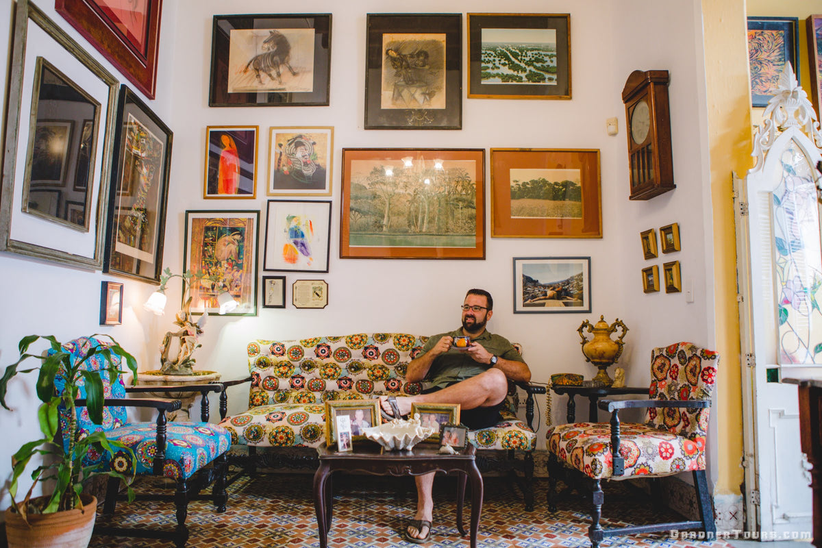 Gardner Tours Owner and Tour Guide Colby Gardner drinking coffee as he sits in a Colorful Living Room with Paintings and Tiled Floors at a Private BnB in Havana, Cuba