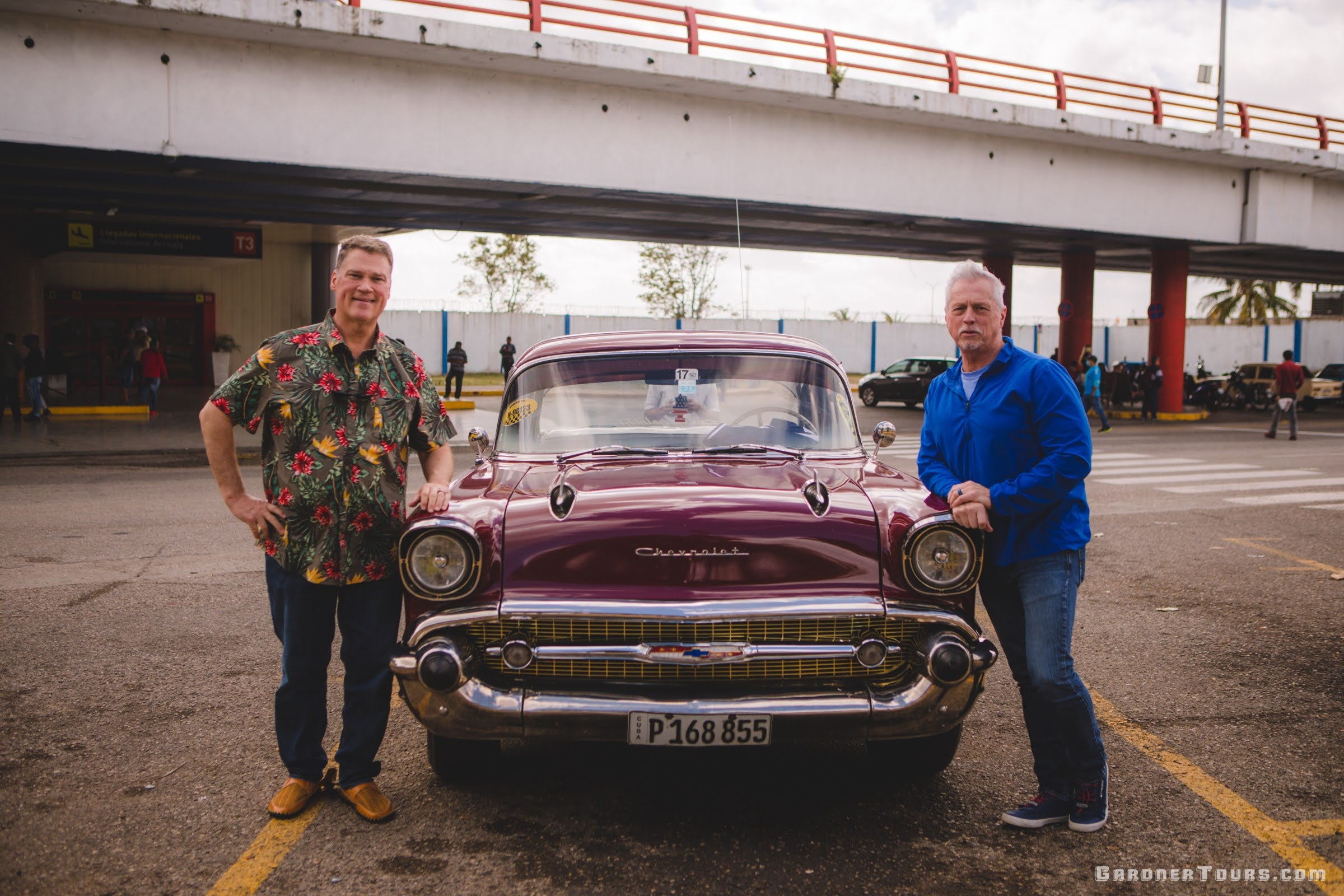 Two American Travelers to Cuba standing by of a Maroon 1957 Chevrolet Bel Air in front of the José Martí International Airport in Havana Cuba