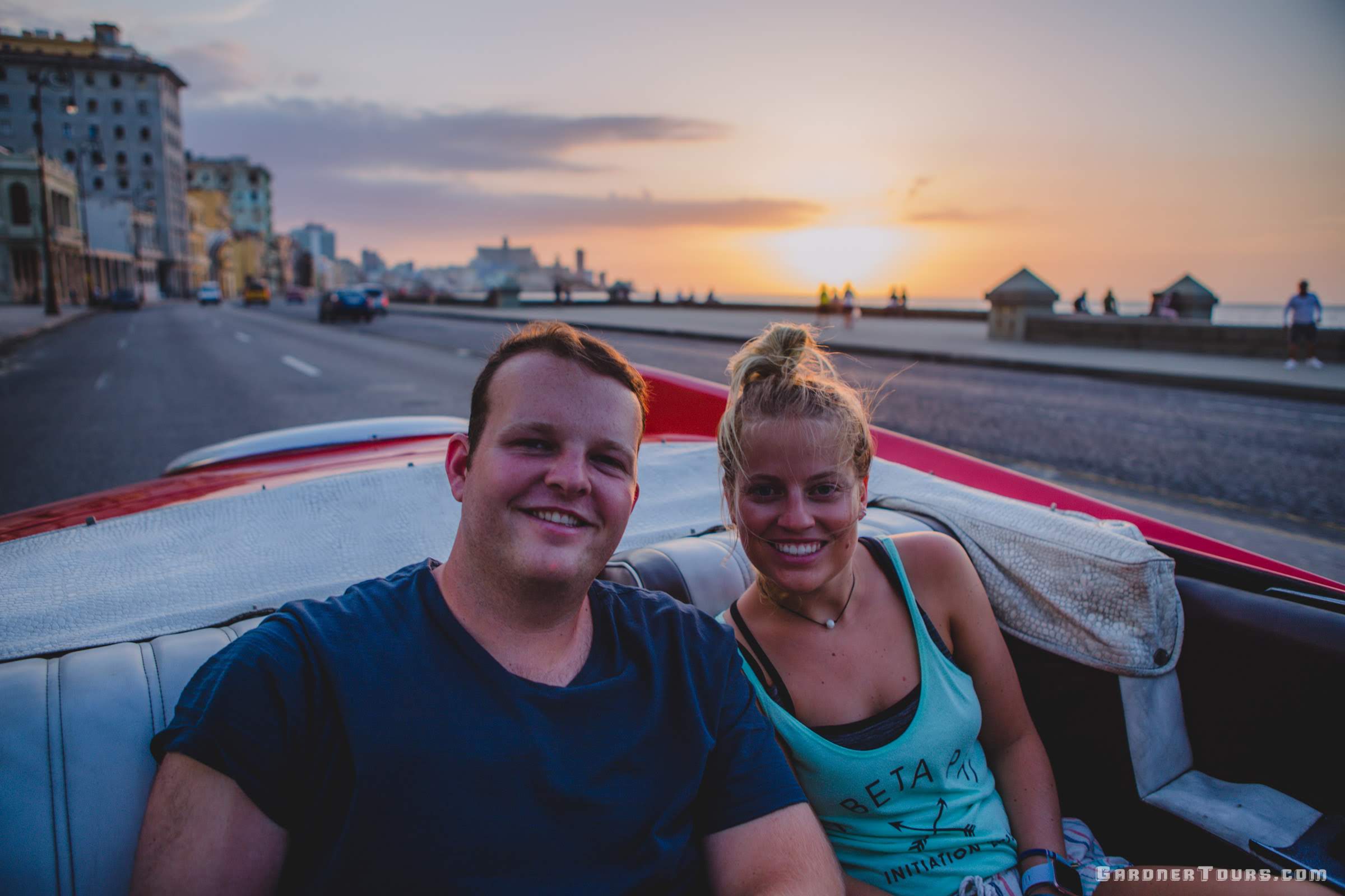 Man and Woman Cruising down the Malecon at sunset in Havana on Classic Car Tour in Classic American Car
