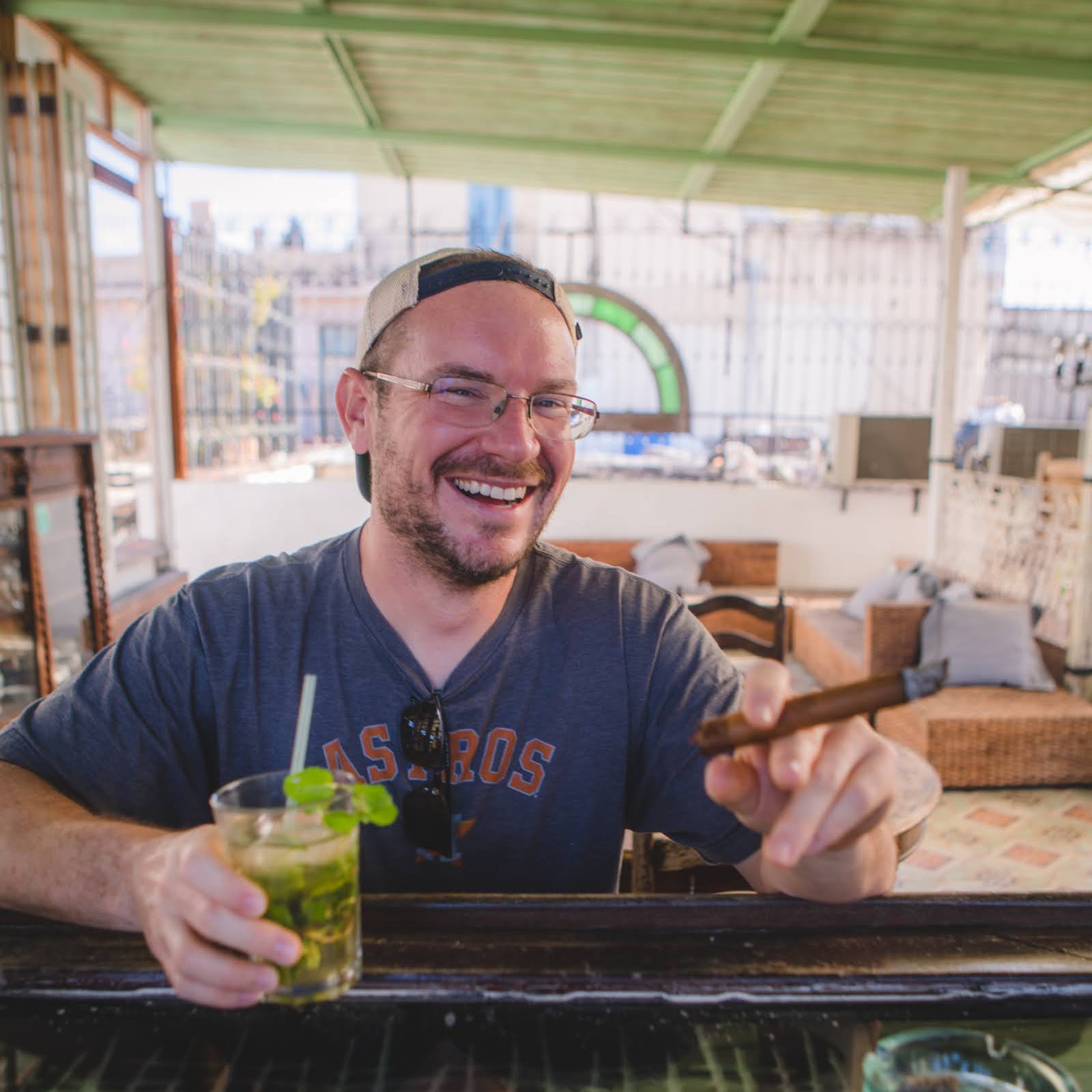Gardner Tours Cuba Tours Man drinking Cuban Mojito and Smoking a Cuban Cigar at a Rooftop Bar in Havana Cuba