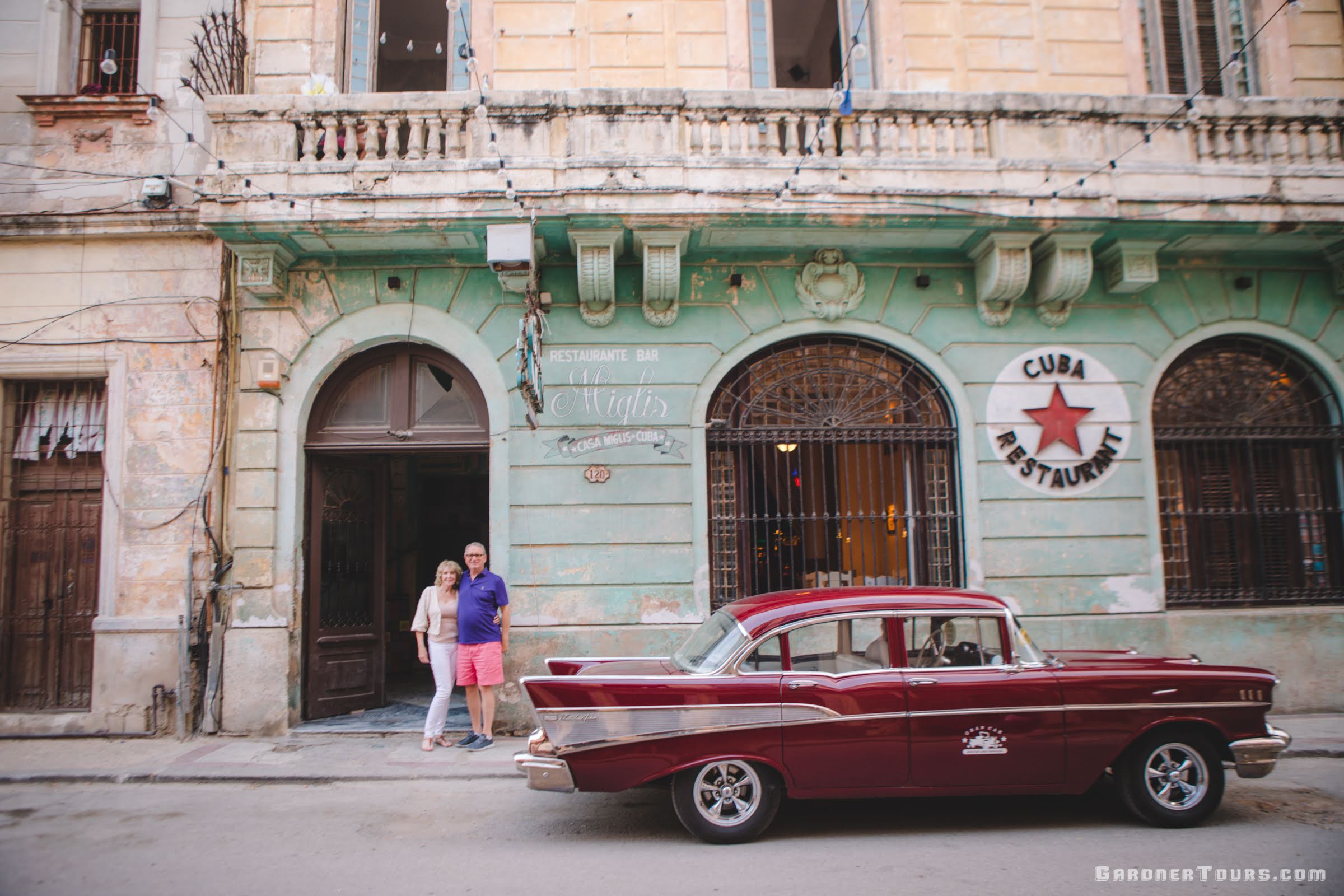Gardner Tours Havana Luxury Tour Hospitality with Elderly Couple Posing by their Maroon 1957 Chevrolet Bel Air in front of Restaurant Casa Miglis in Central Havana Cuba