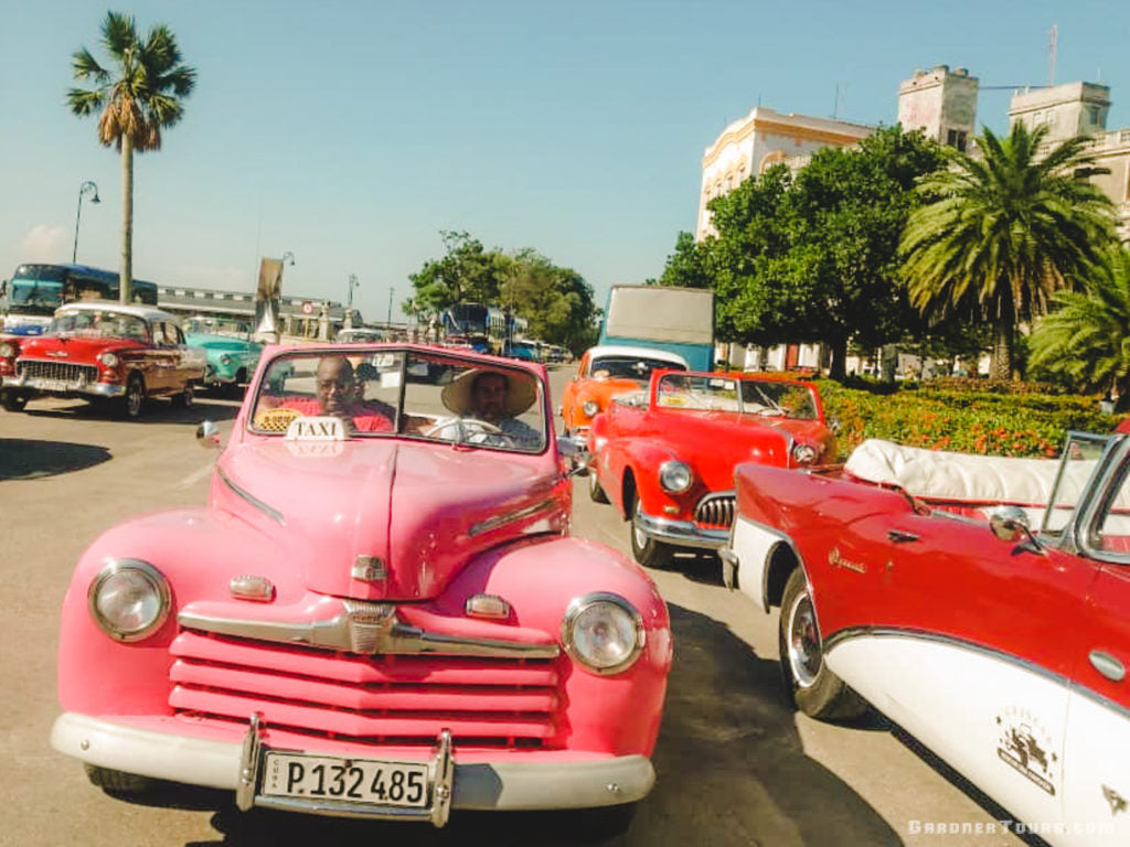 Gardner Tours Cuban Tour Guide Carlos in a pink classic convertible with his travelers on a Classic Car Tour in Havana, Cuba