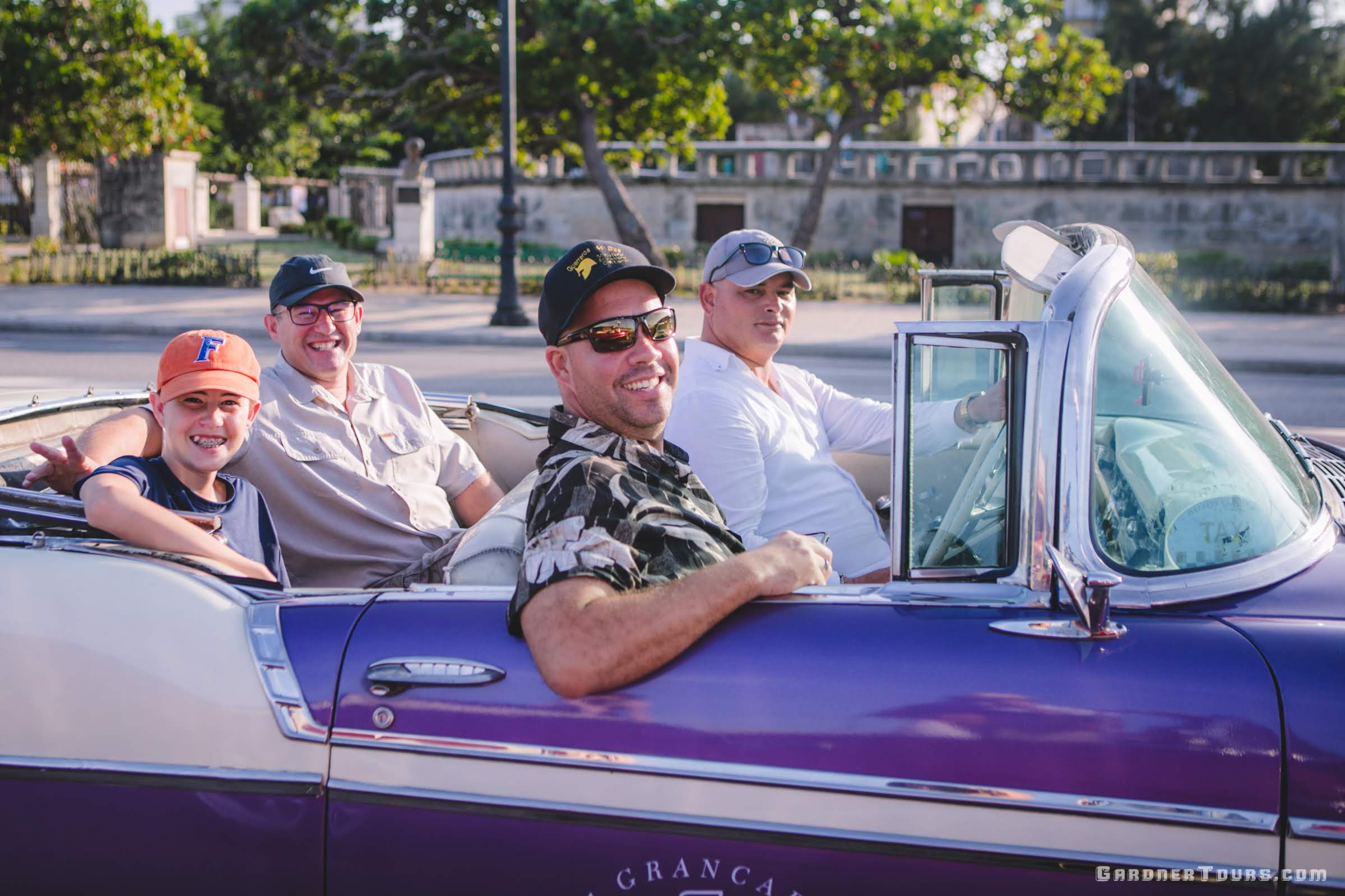 Gardner Tours Cuban Tour Guide Yunior riding in a purple car with two American travelers on a Classic Car Tour in Havana, Cuba