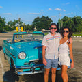 Couple enjoying a Custom Havana Day Tour with Gardner Tours, standing beside a classic blue 1954 Mercury in Havana, Cuba.