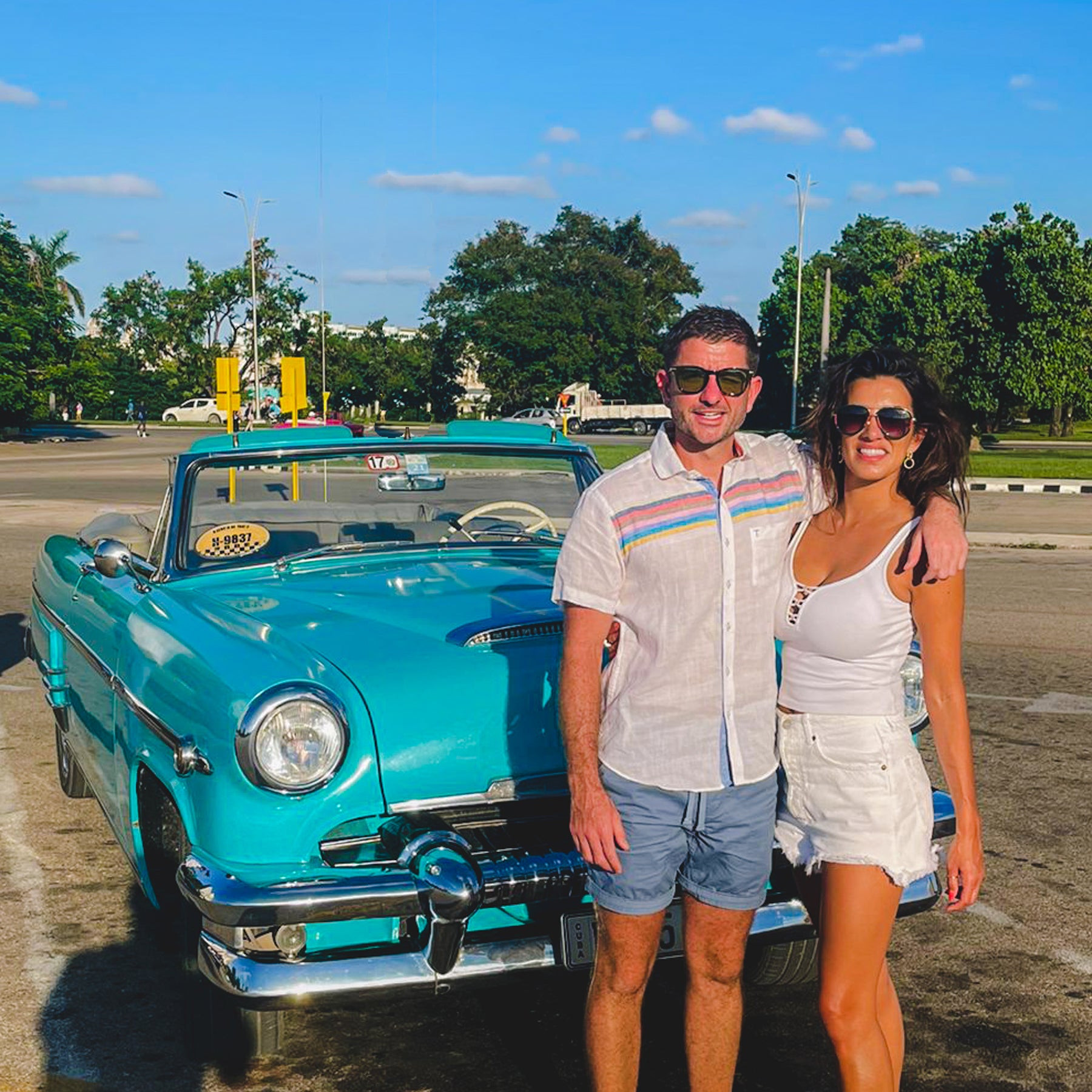 Couple enjoying a Custom Havana Day Tour with Gardner Tours, standing beside a classic blue 1954 Mercury in Havana, Cuba.