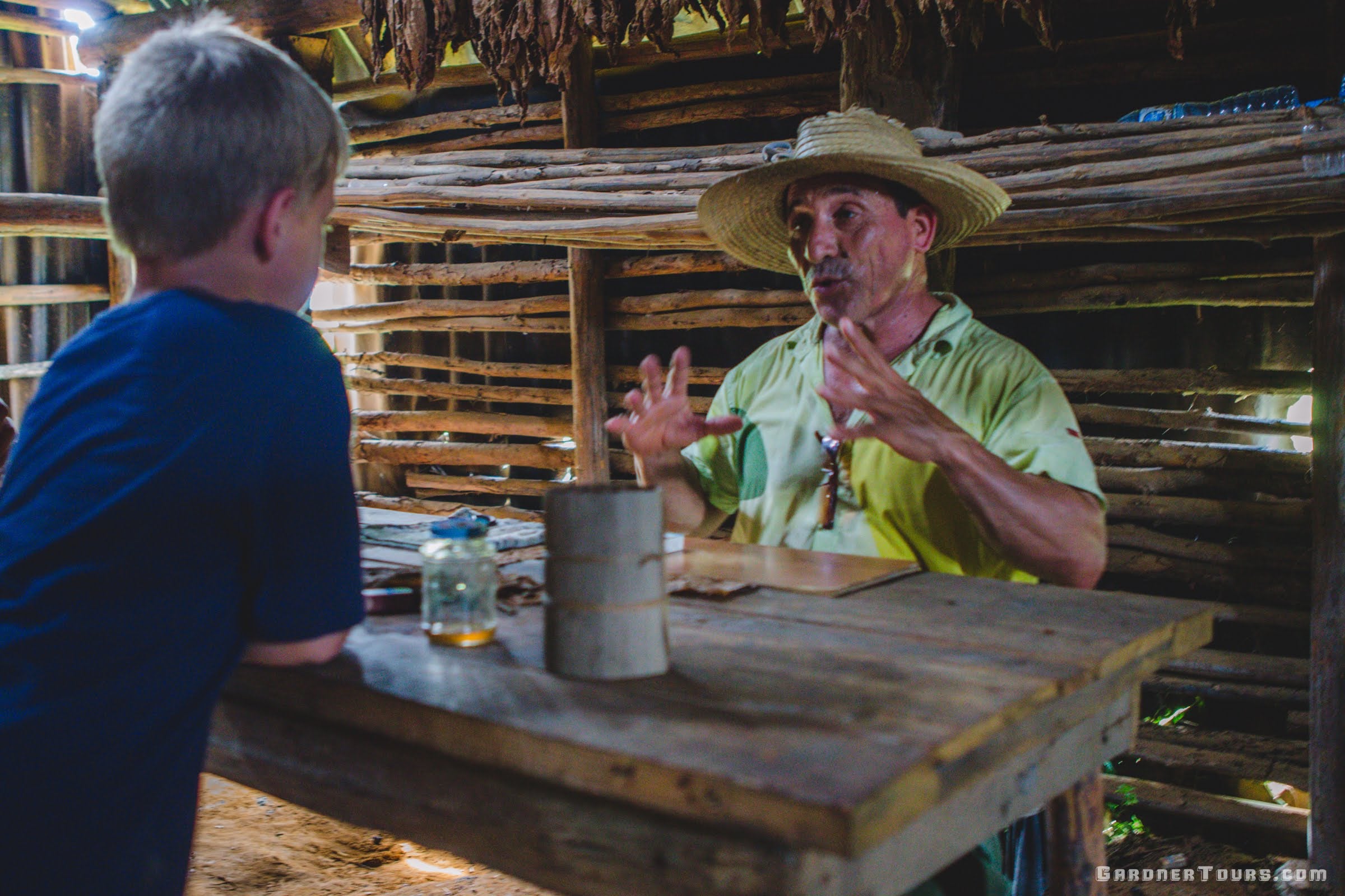 A trusted local Cuban farmer in a traditional hat sharing his craft with a young traveler, illustrating Gardner Tours' commitment to local empowerment and authentic community investment.