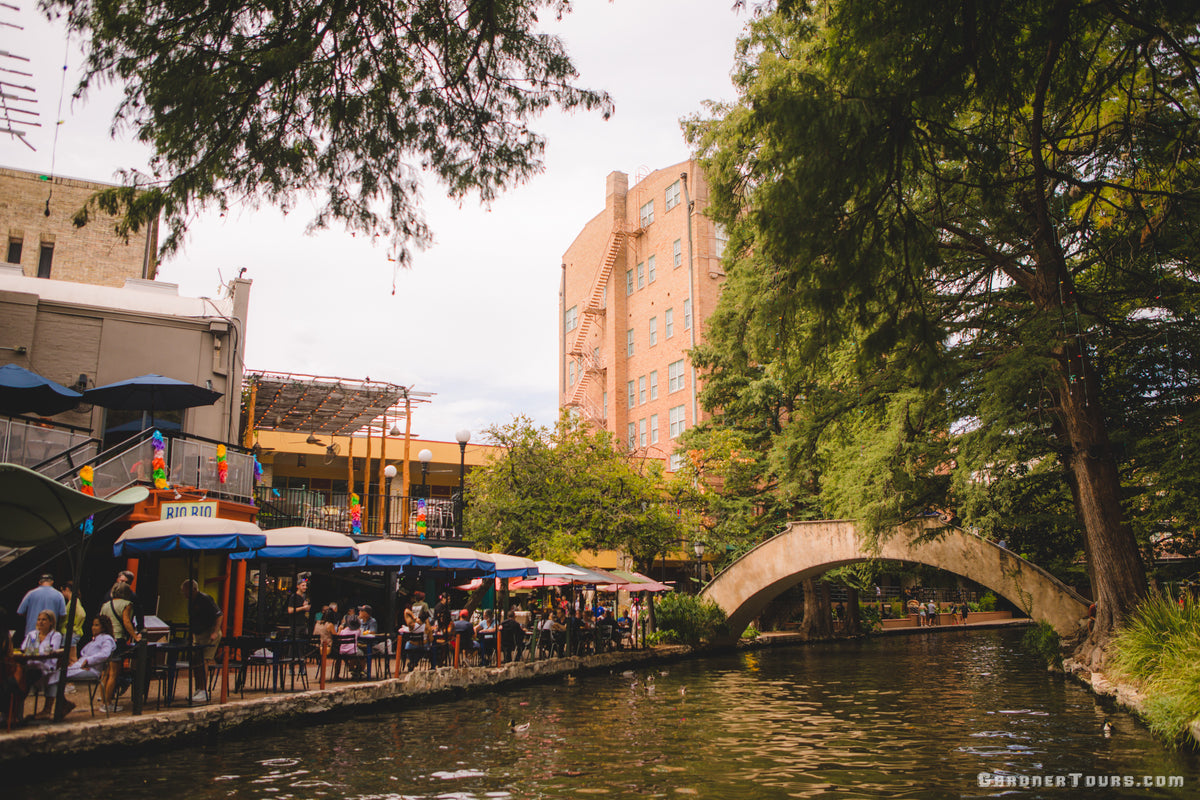 View of the San Antonio River Walk with its charming bridge and colorful riverside scenery featured on the Gardner Tours Texas Traditions Tour.