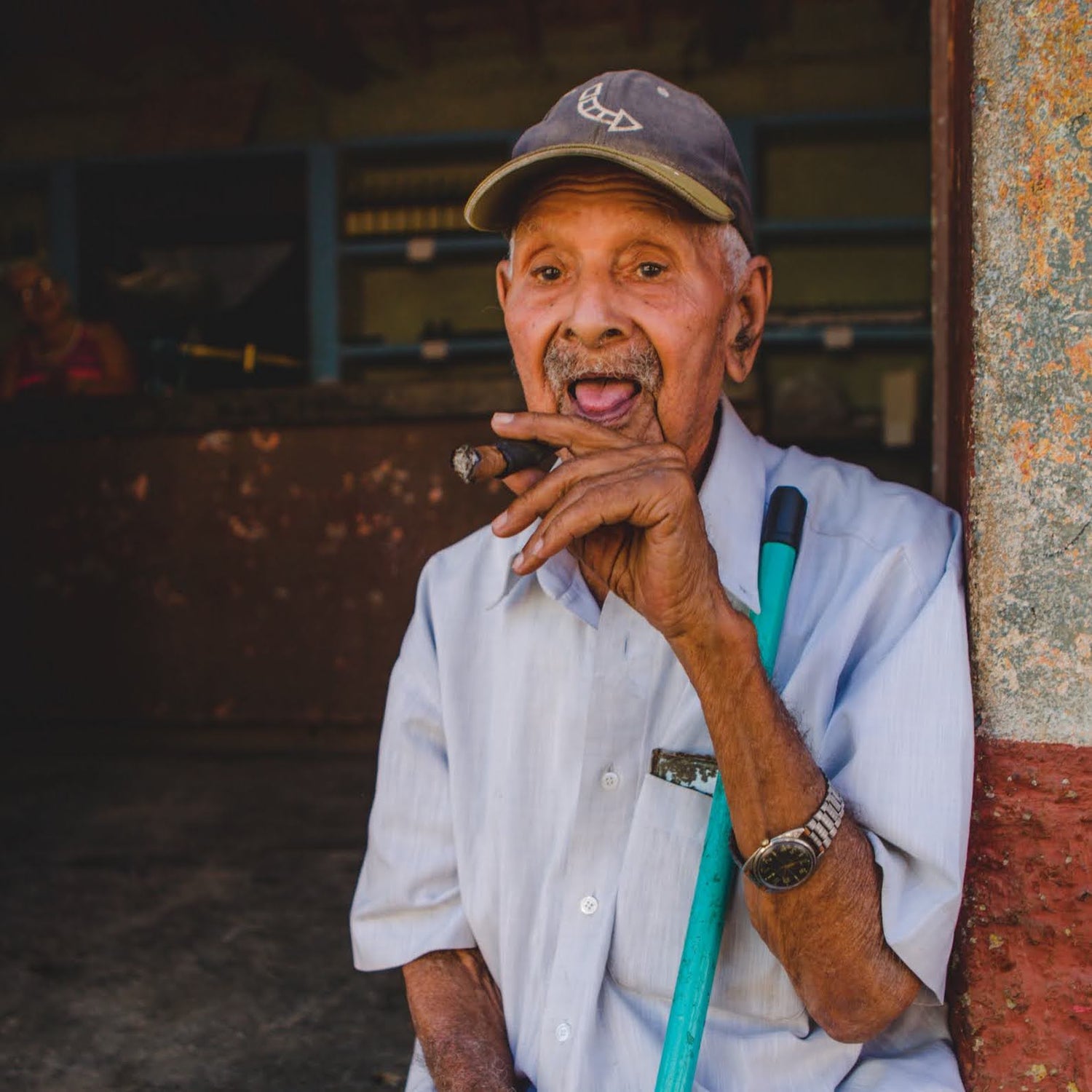A portrait of an elderly Cuban man sitting in a doorway, holding a cigar and smiling, representing the authentic local culture of Cuba.